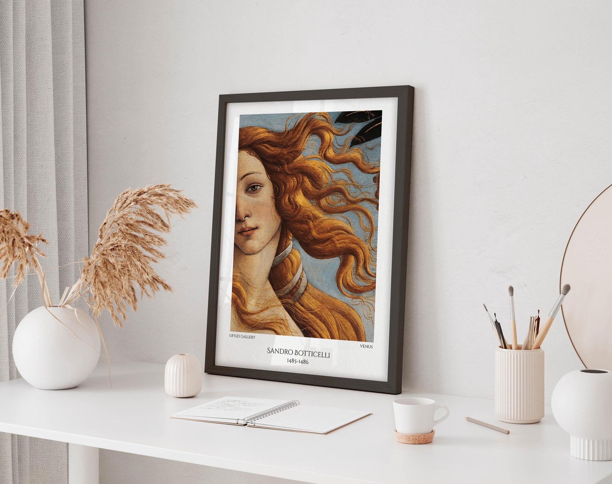 a framed painting of a woman with flowing hair, displayed on a white desk. The desk also has various items such as a notebook, a cup, and a vase.