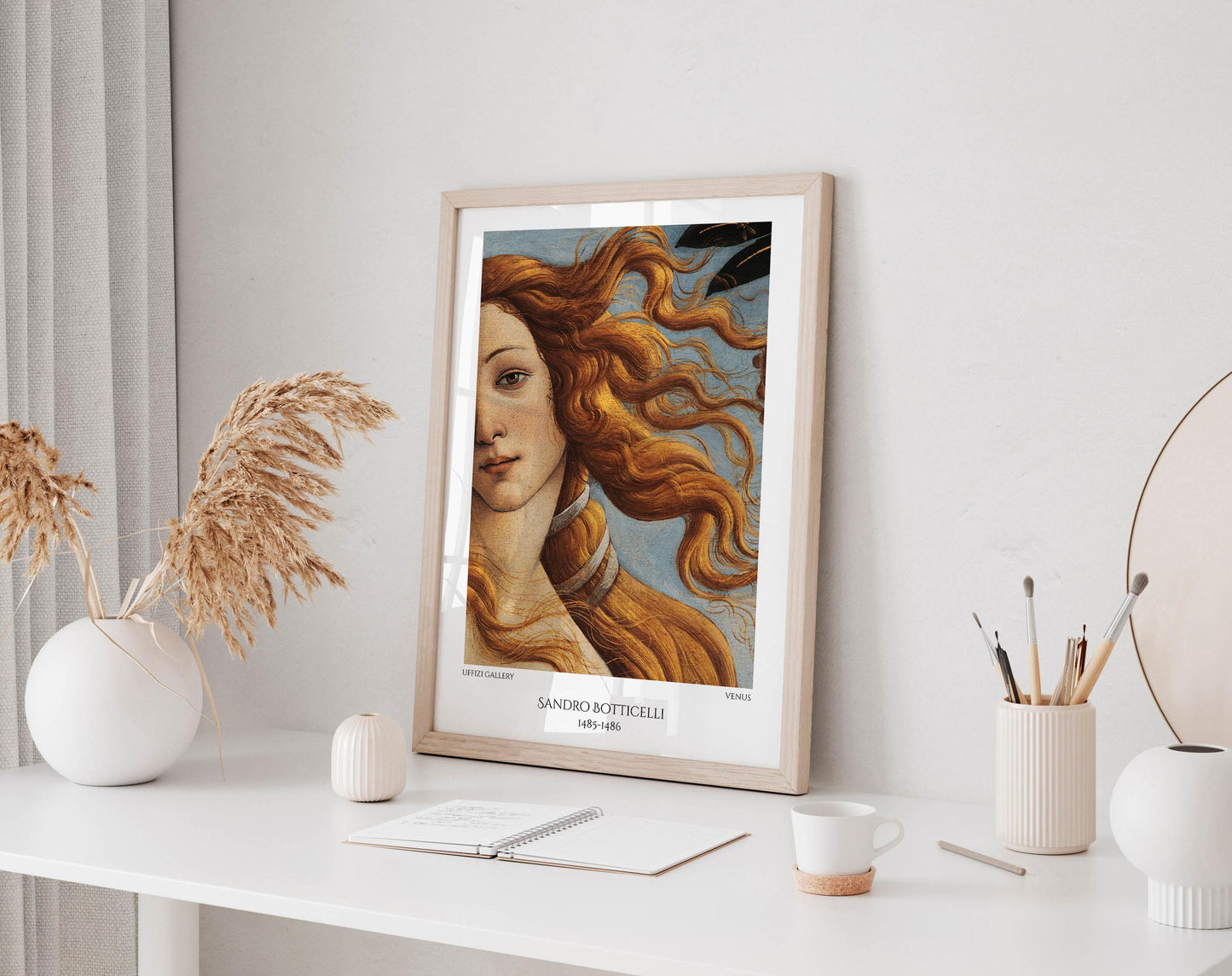 a framed painting of a woman with flowing hair, displayed on a white desk. The desk also has various items such as a notebook, a cup, and a vase.
