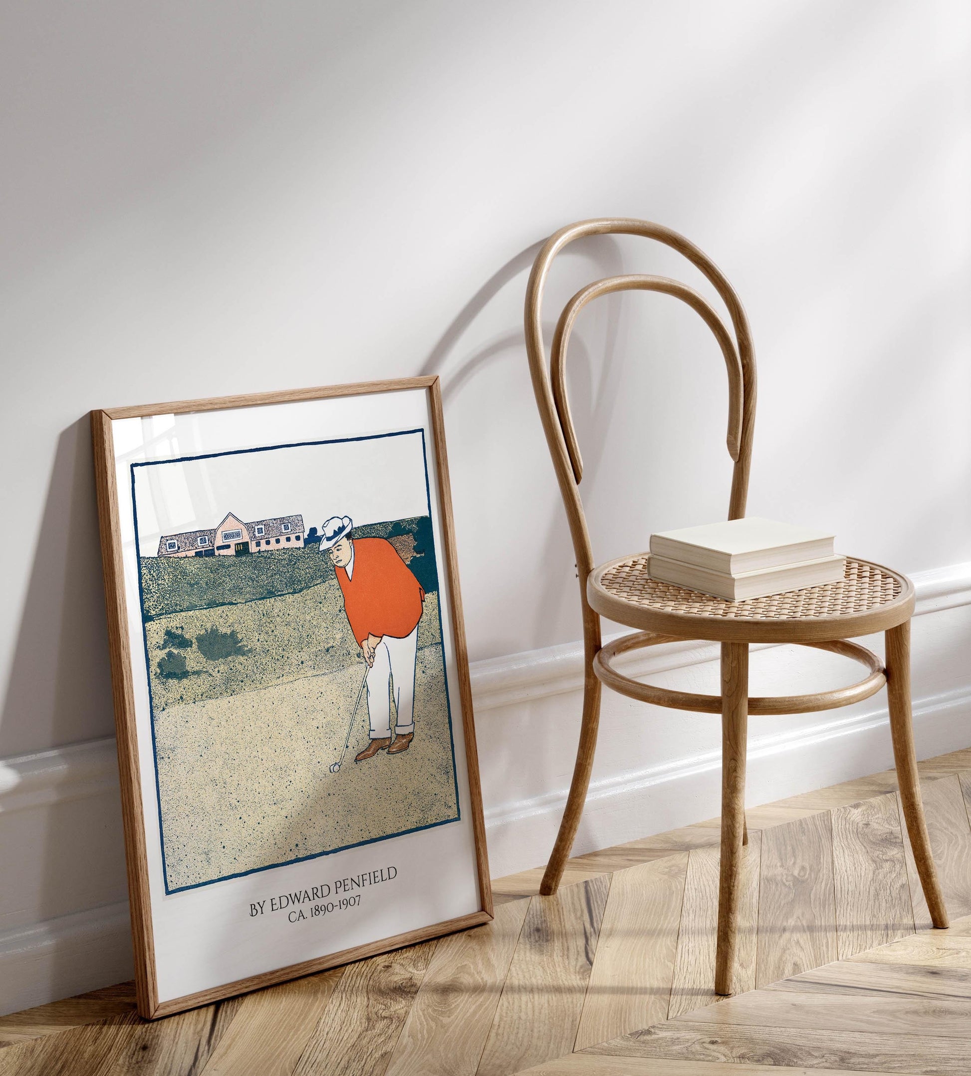 a framed illustration of a golfer on a golf course, with a chair and a book on a wooden floor next to it.
