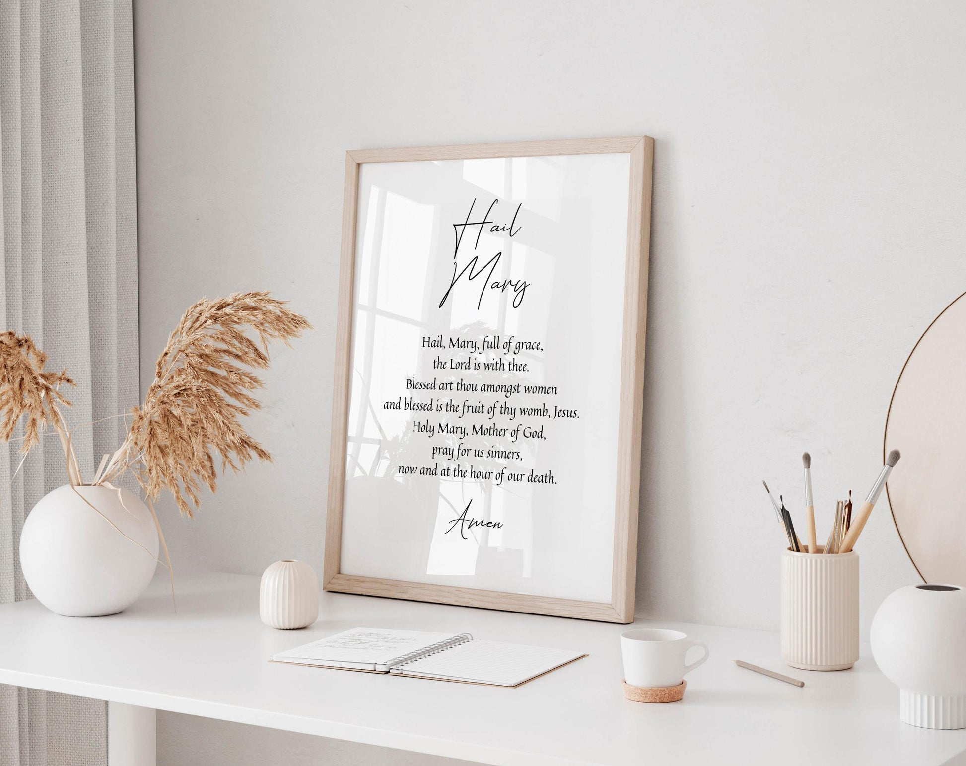 a framed quote on a white wall, surrounded by various objects such as a white vase, a notebook, a cup, and a pencil holder.