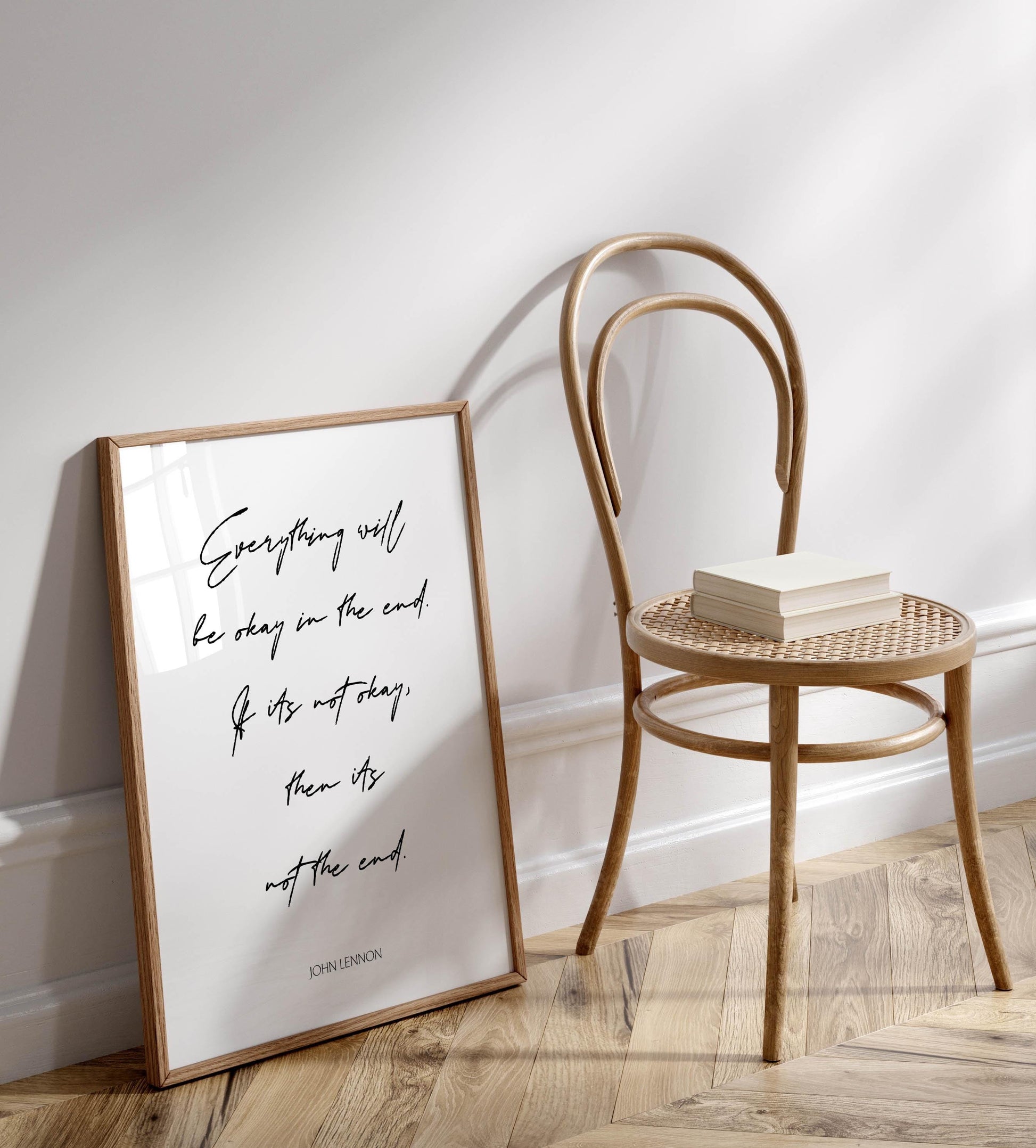 a framed quote by John Lennon, "Everything will be okay in the end if it's not too late," placed next to a wooden chair on a wooden floor.