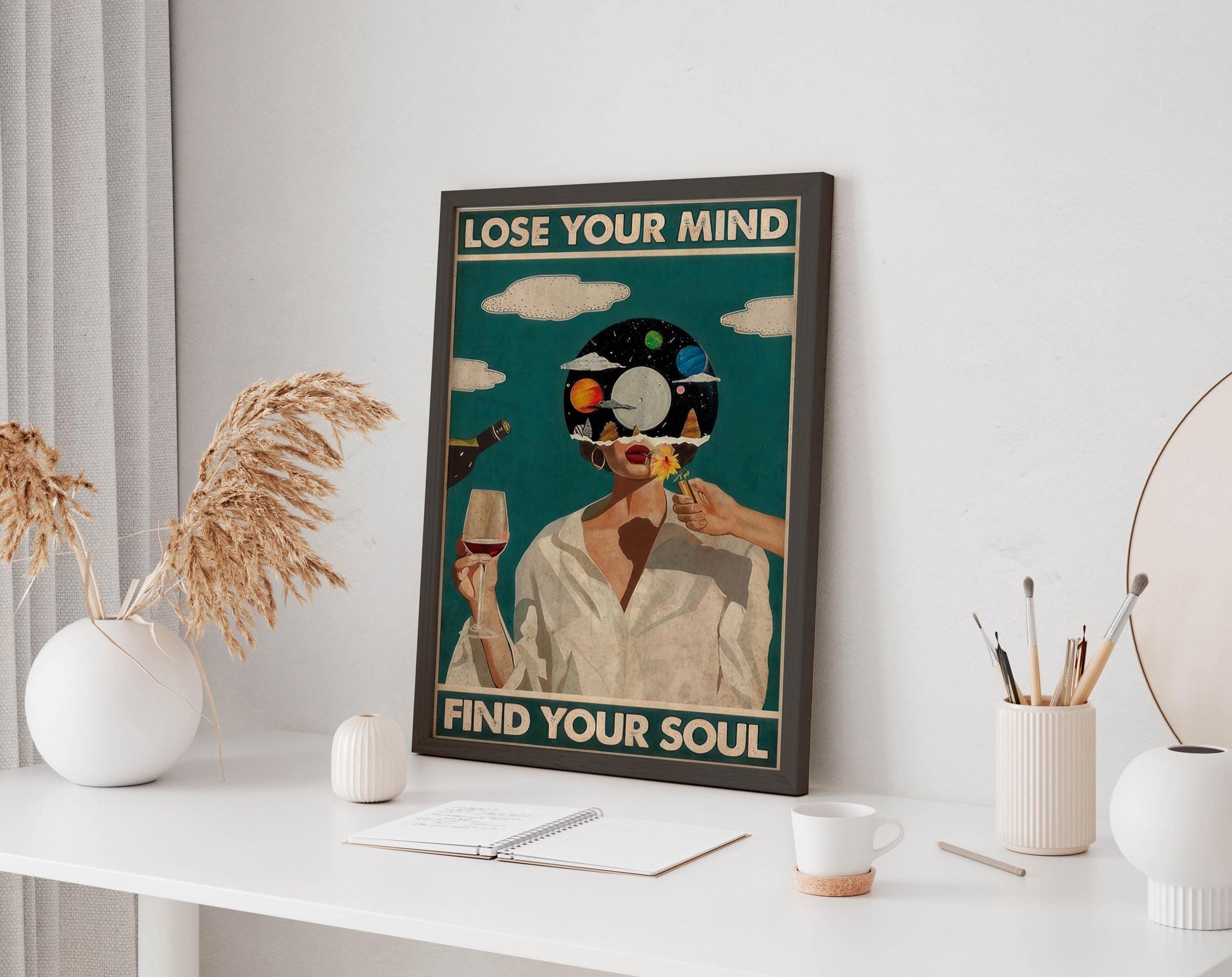 a framed poster with the text "LOSE YOUR MIND FIND YOUR SOUL" displayed on a white wall above a desk with various items on it, including a notebook, a cup, and a vase.