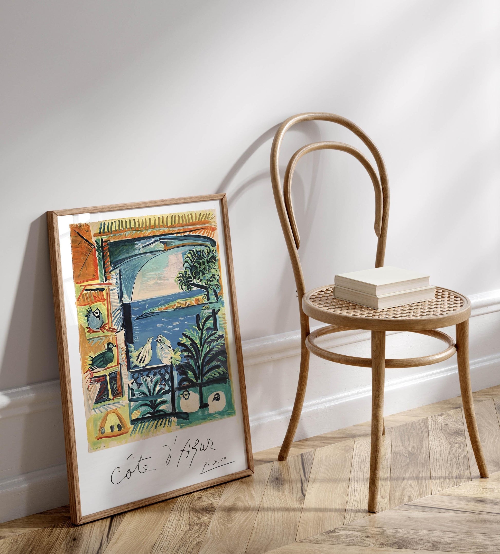 a wooden chair with a book resting on it, positioned next to a framed painting on a wall.