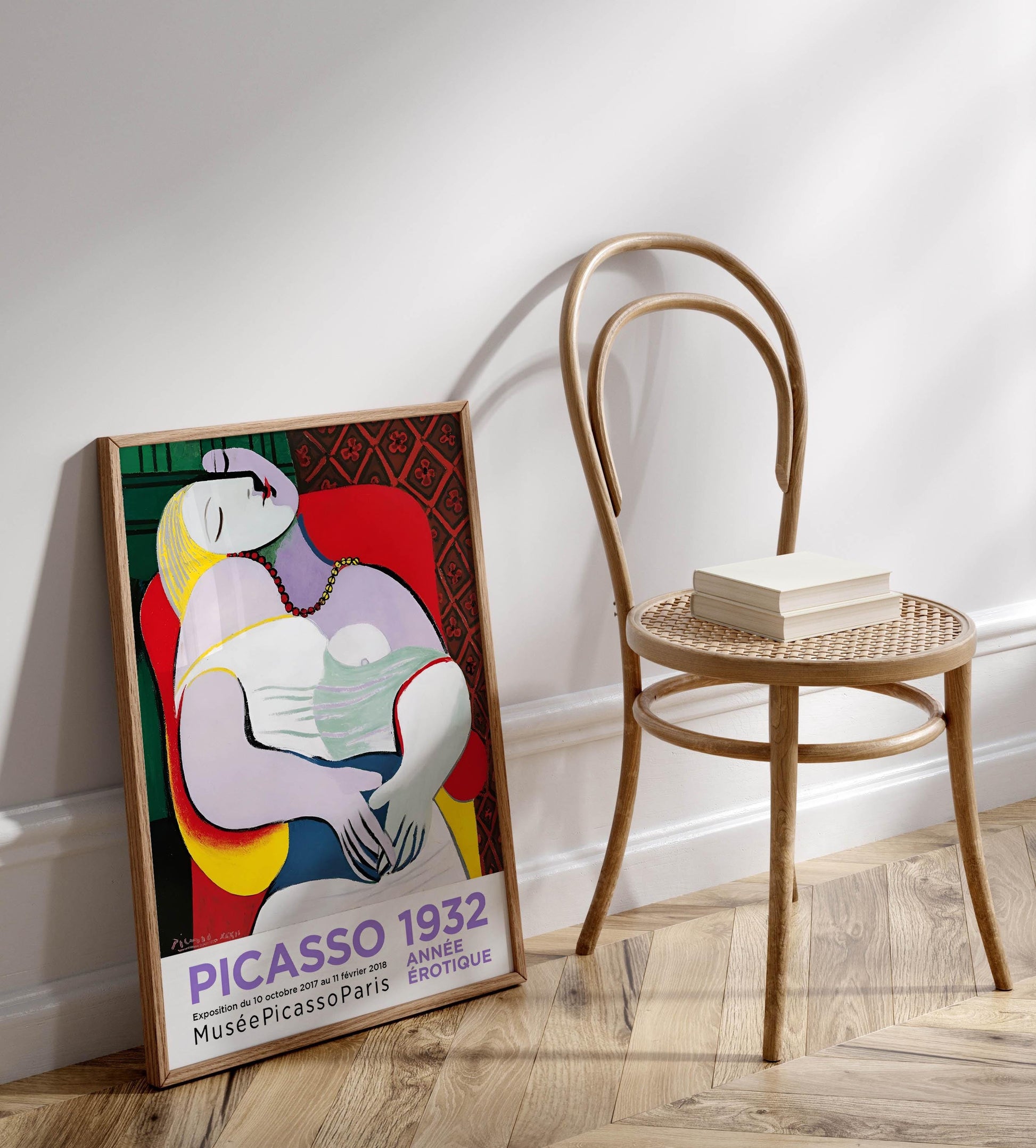 a colorful Picasso 1932 poster displayed on a wall next to a wooden chair.