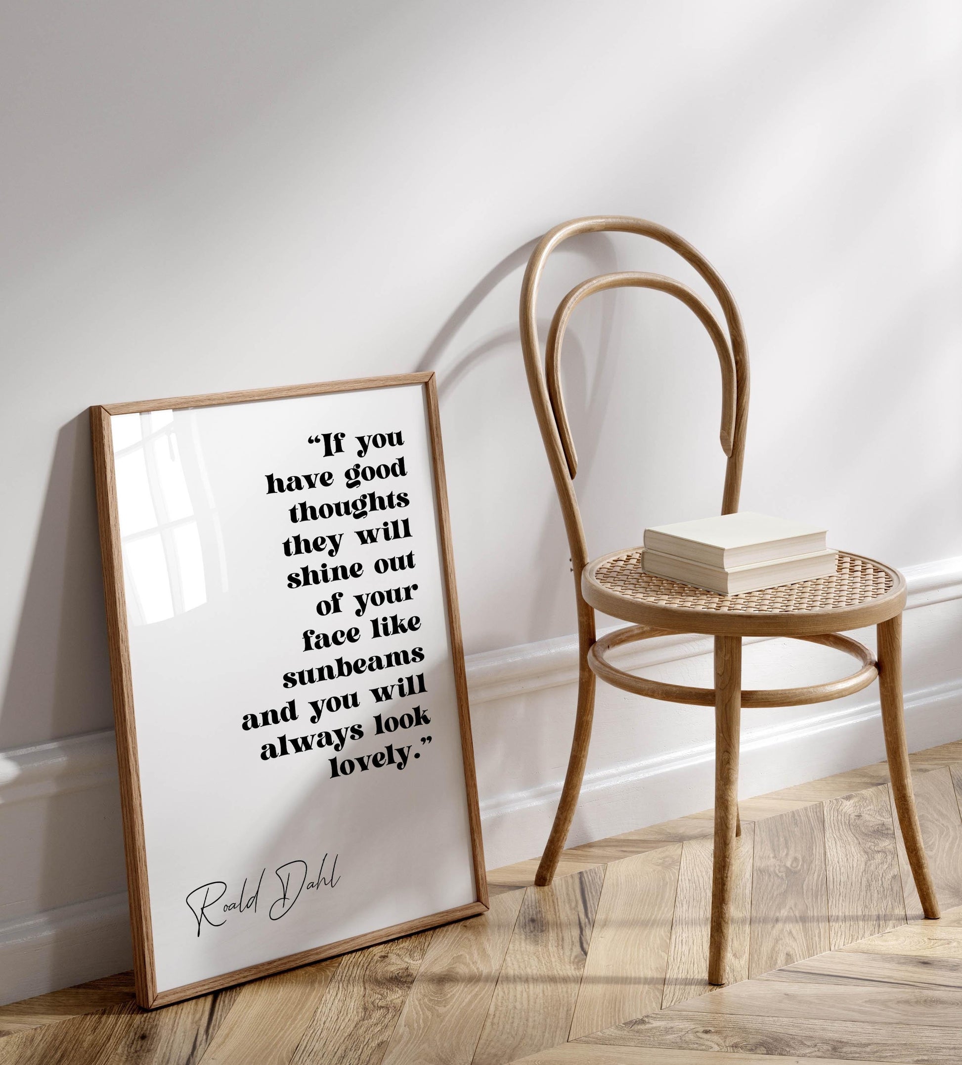 a framed quote by Ralph Dahl, "If you have good thoughts they will shine out of your face like sunbeams and you will always look lovely." The quote is displayed on a white wall, with a wooden chair positioned next to it.
