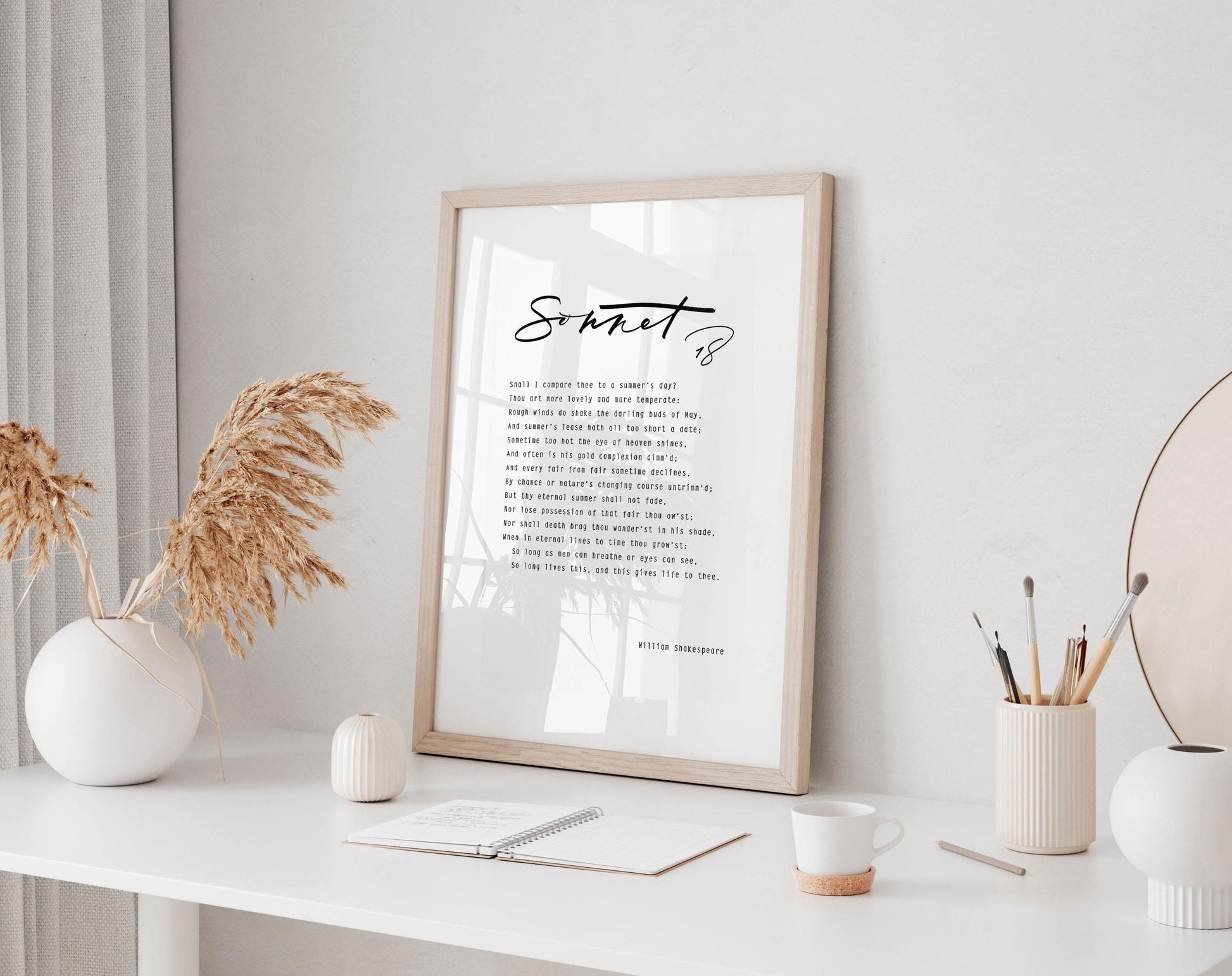 a framed quote on a white desk, surrounded by various objects such as a notebook, a cup, and a vase with dried flowers.