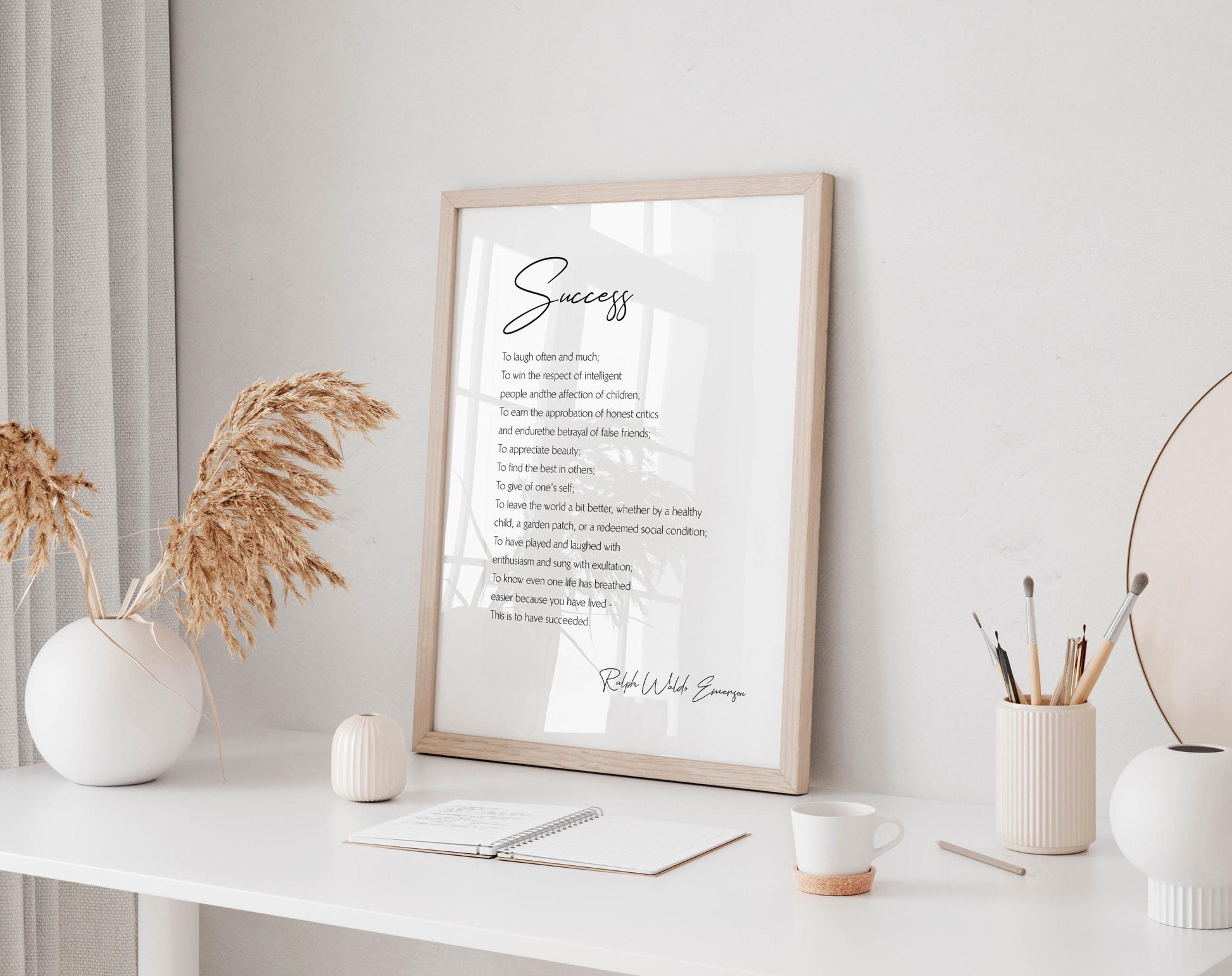 a framed motivational quote, a white desk with various items such as a notebook, a cup, and a vase, and a window with a plant.