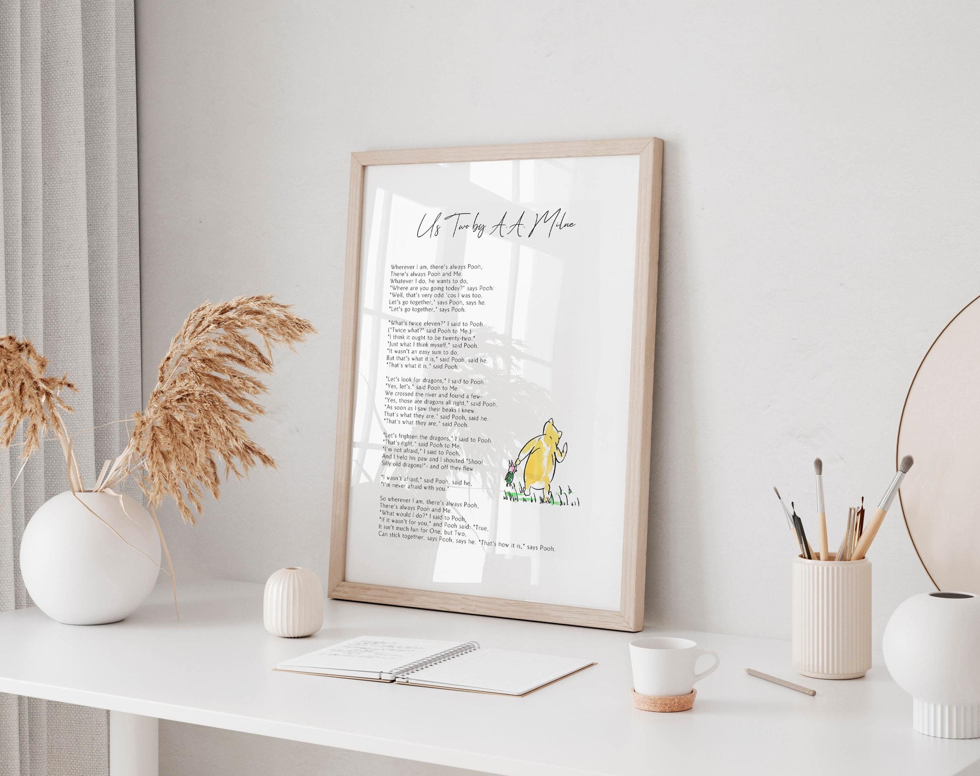 a framed poem titled "Us Two by a Moo" on a white desk, surrounded by various objects such as a notebook, a cup, a vase, and a potted plant.