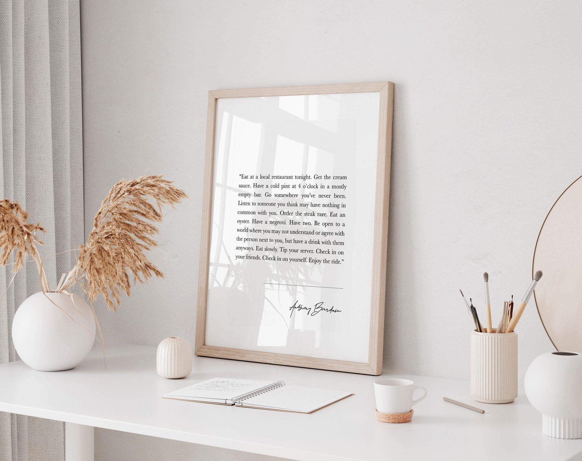 a framed quote on a white shelf, surrounded by various objects such as a white vase, a white candle, and a white mug.