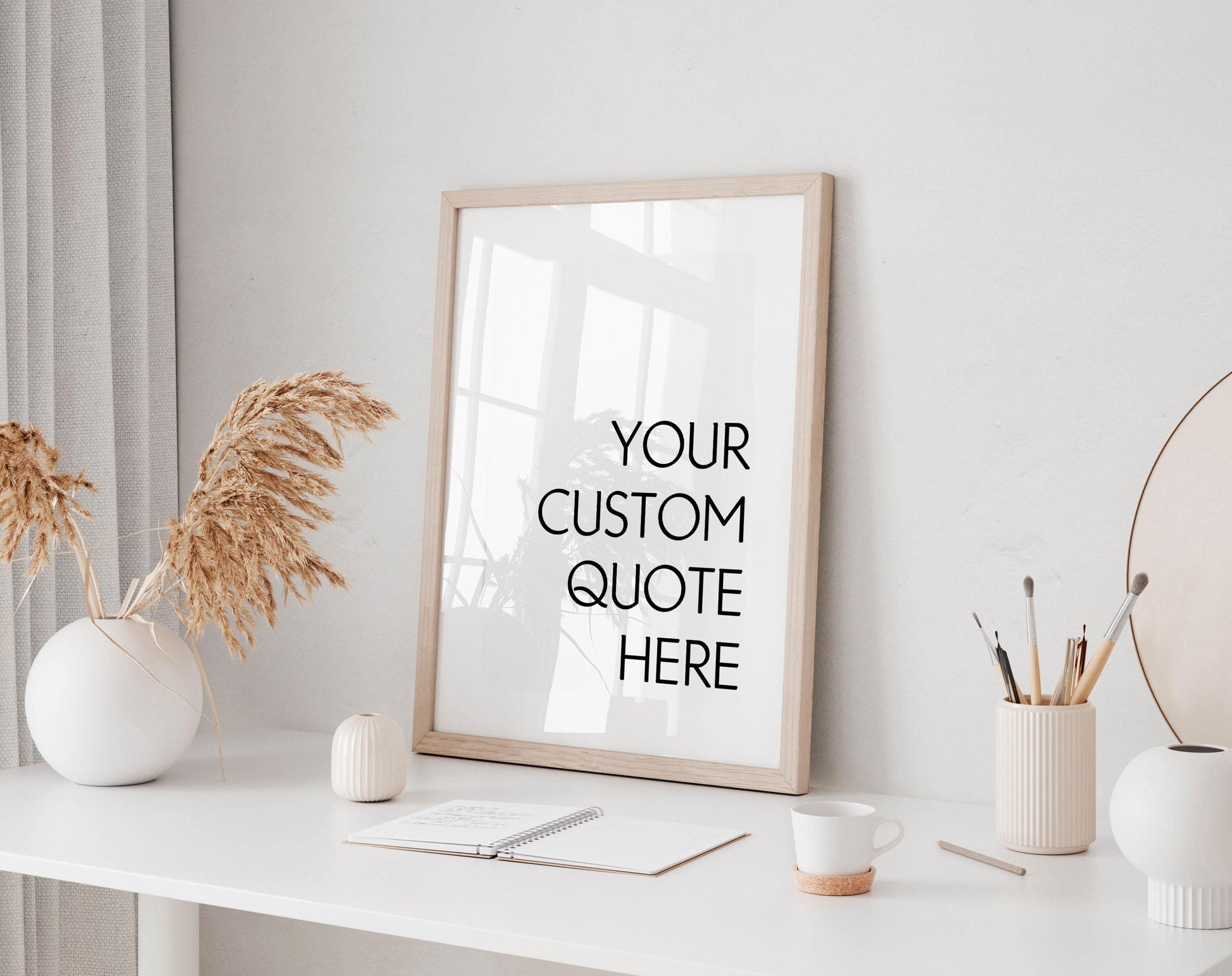 a white desk with a framed quote, a notebook, a cup, and a vase with dried flowers.