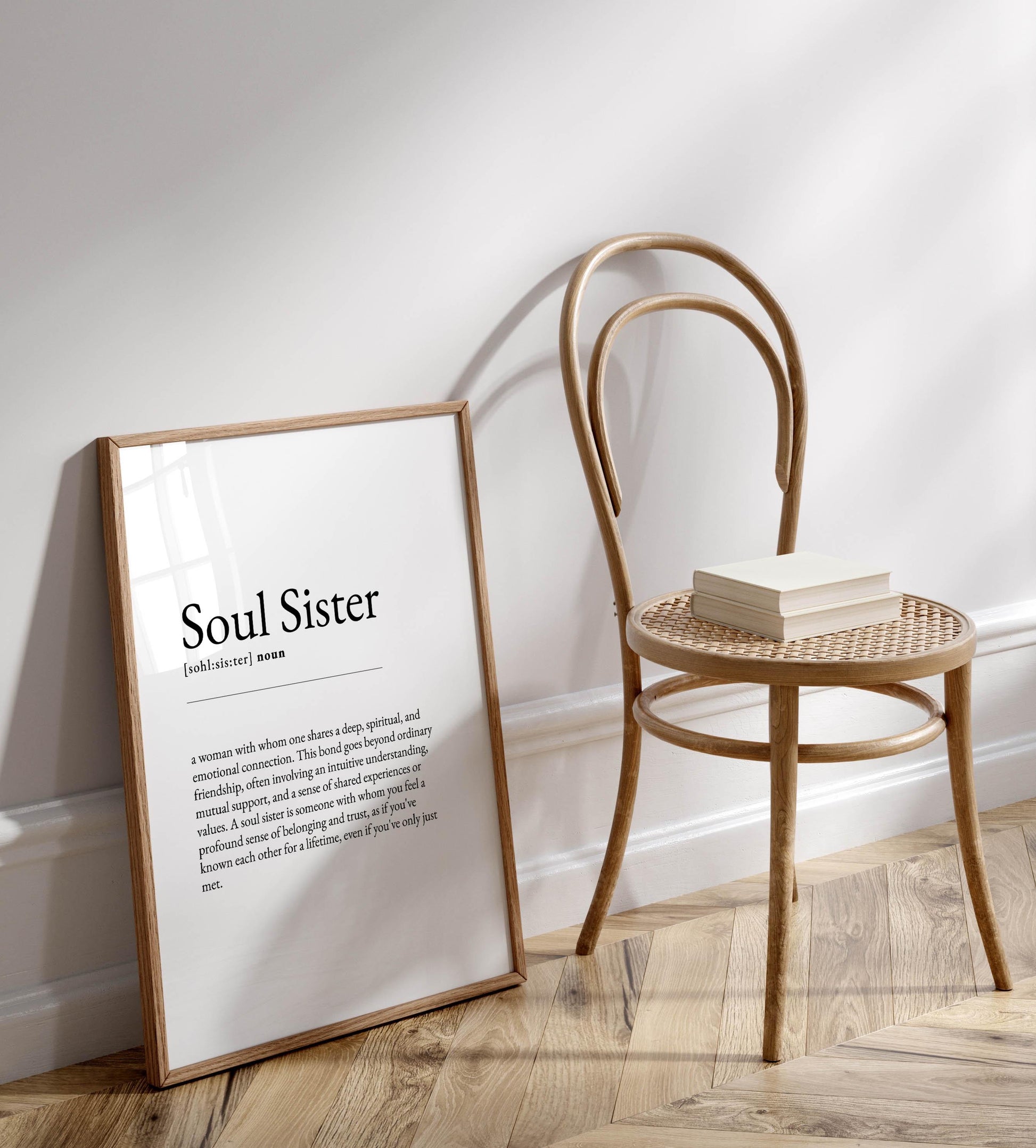 a wooden chair with a book on it, placed against a white wall. There is a framed definition of "Soul Sister" next to the chair.