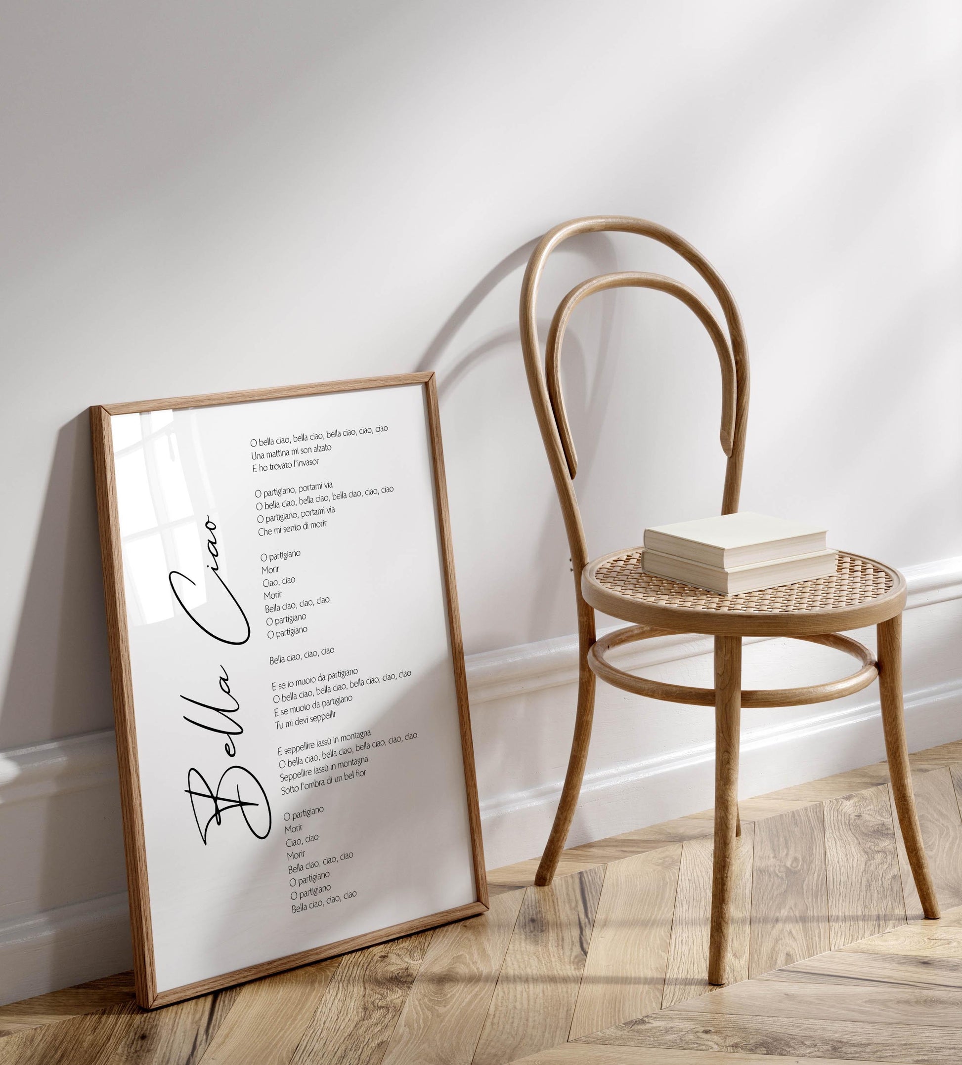 a wooden chair with a framed text poster or sign leaning against it, which appears to be a song or lyrics. The poster is placed on a wooden floor, and there is a stack of books next to the chair.