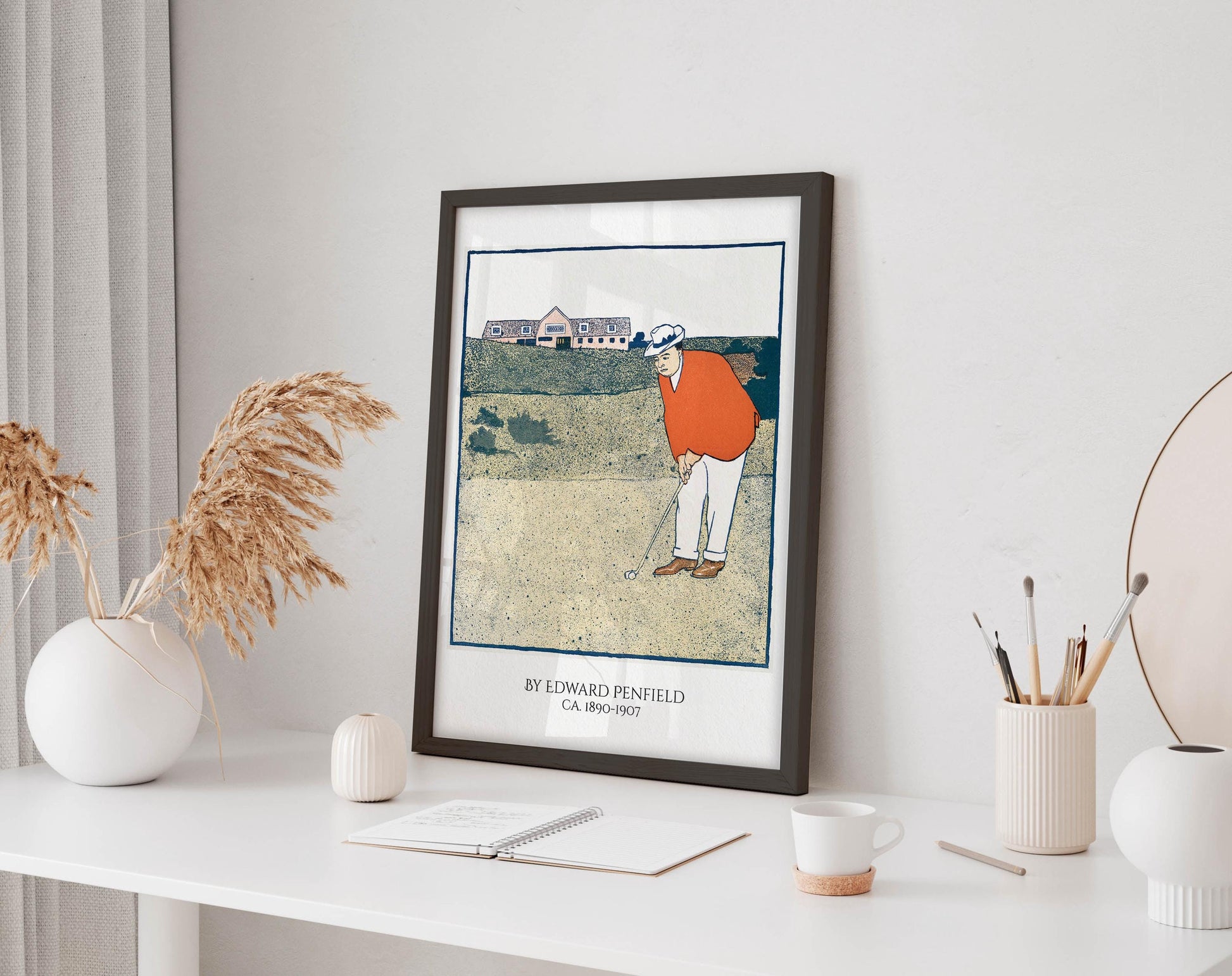 a framed illustration of a golfer on a golf course, with a vase of dried flowers and a cup of coffee on a desk in the foreground.