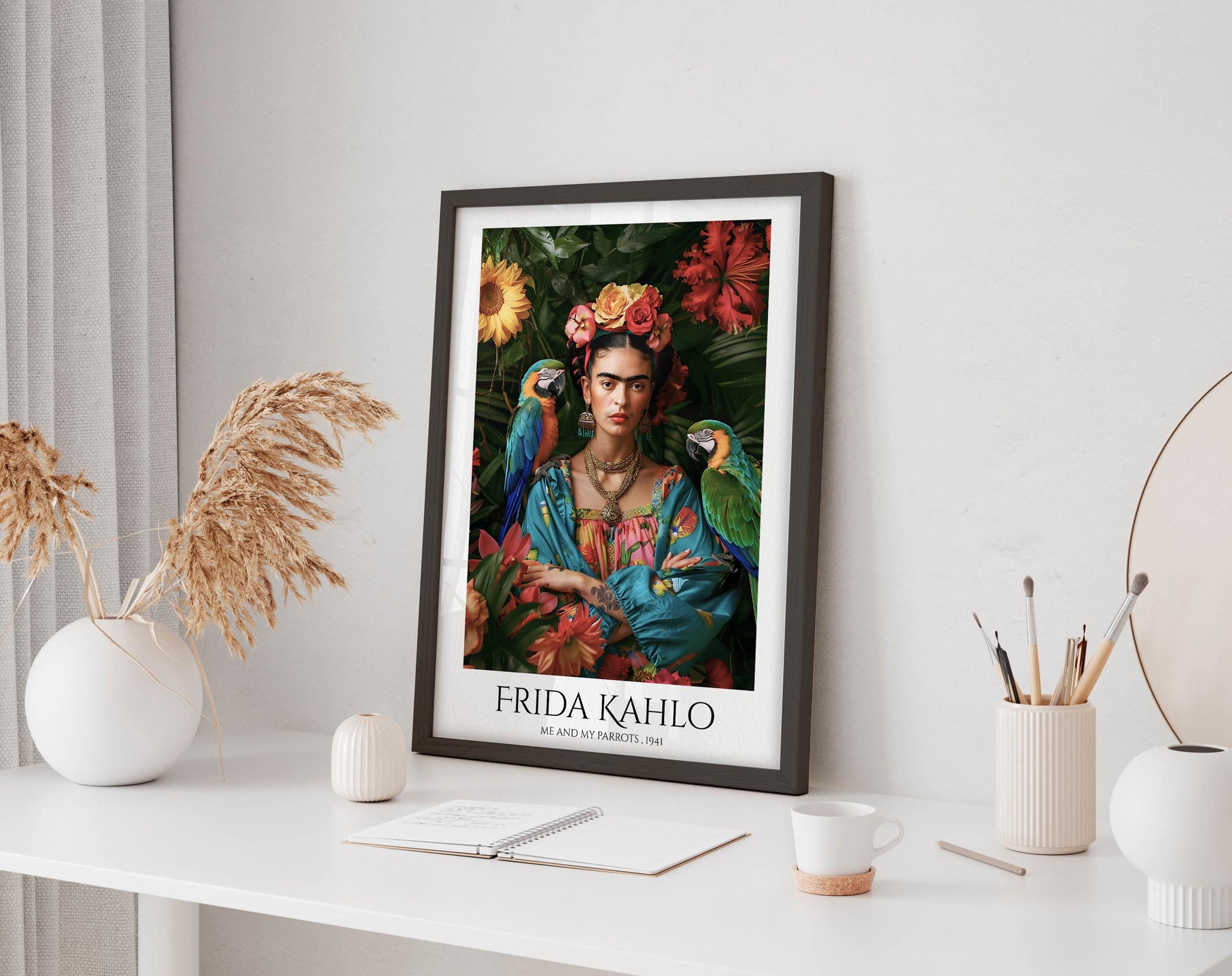 a framed poster of Frida Kahlo, a famous Mexican artist, displayed on a white shelf. The poster is surrounded by various objects, including a white vase, a small white candle, a white mug, and a white notebook.