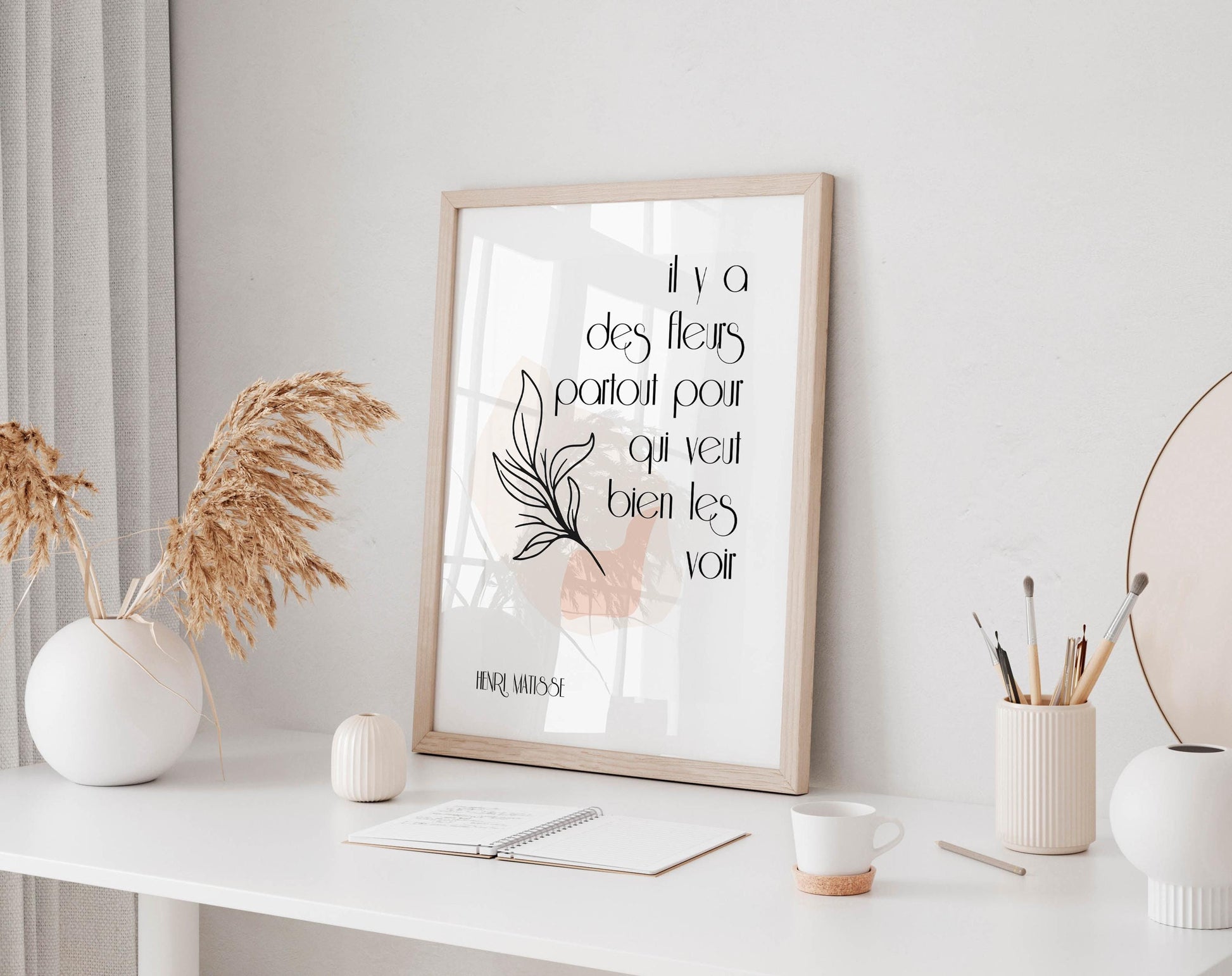 a white desk with a framed quote, a notebook, a cup, and a vase with dried flowers.