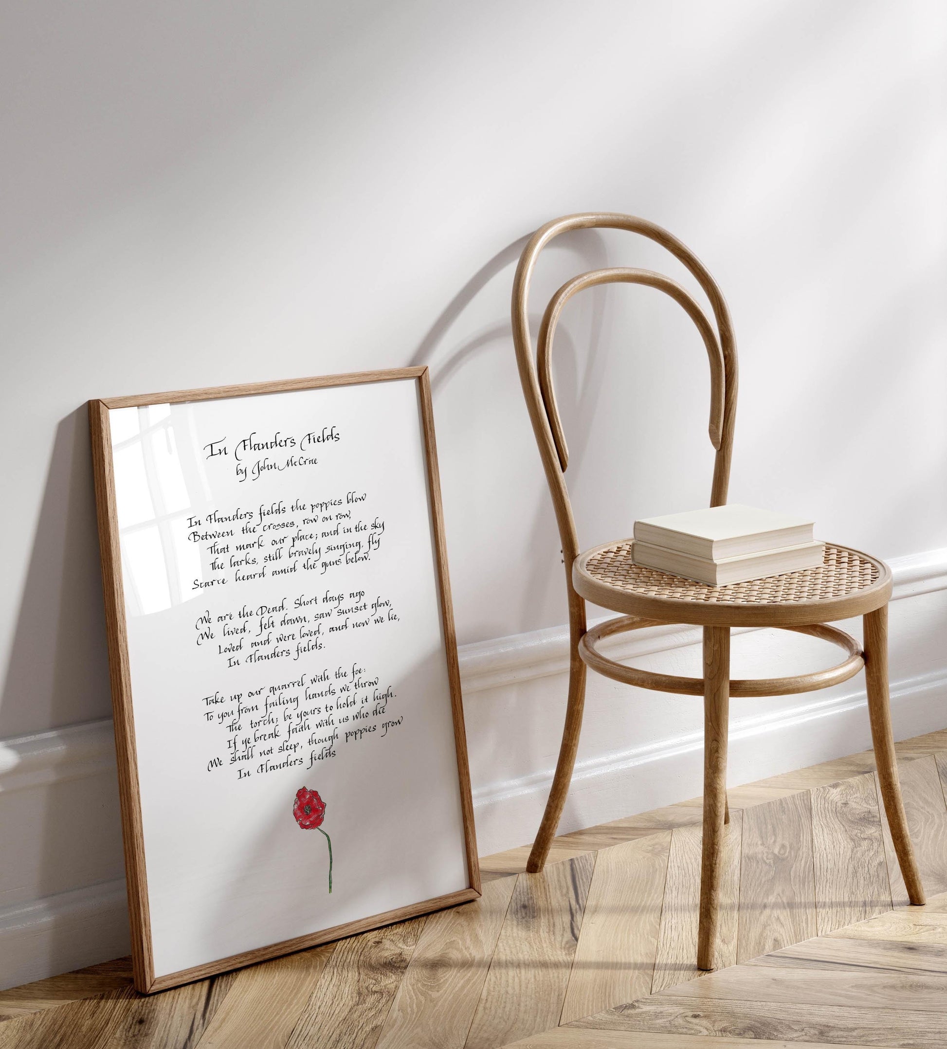 a framed poem titled "In The Clouds" by John McCrae, placed on a wooden floor next to a wooden chair.