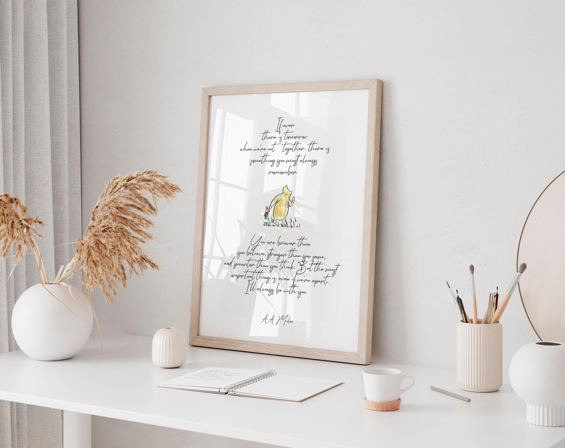 a framed quote with a yellow duck on a white background, placed on a white desk with various items such as a notebook, a cup, and a vase.