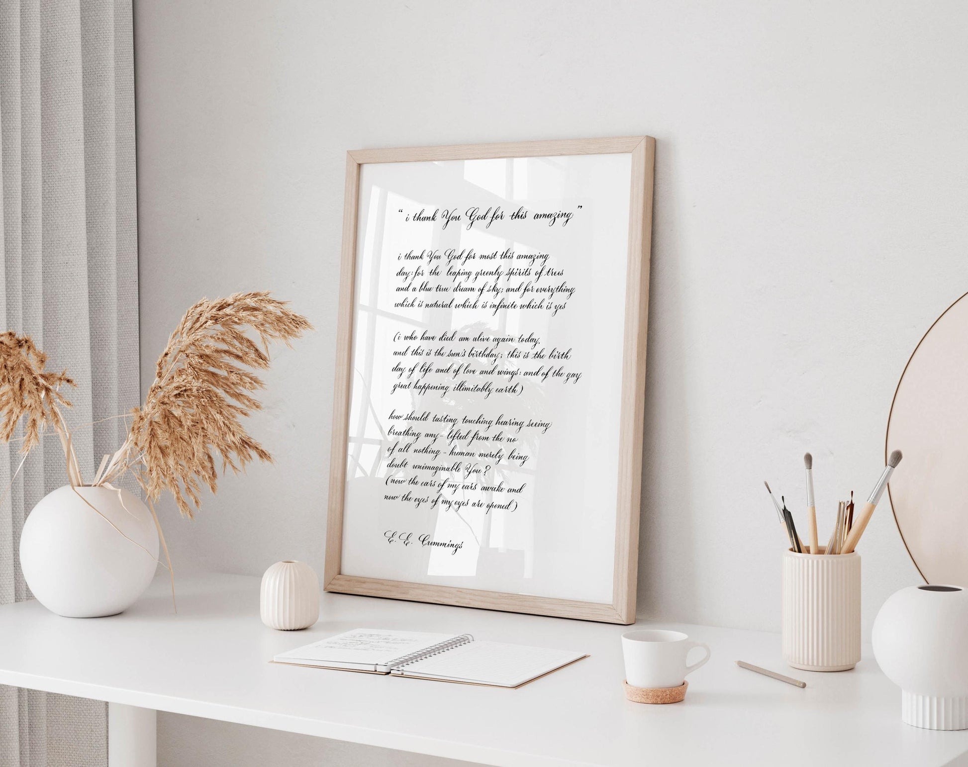 a framed quote on a white desk, surrounded by various objects such as a notebook, a cup, and a vase with dried flowers.