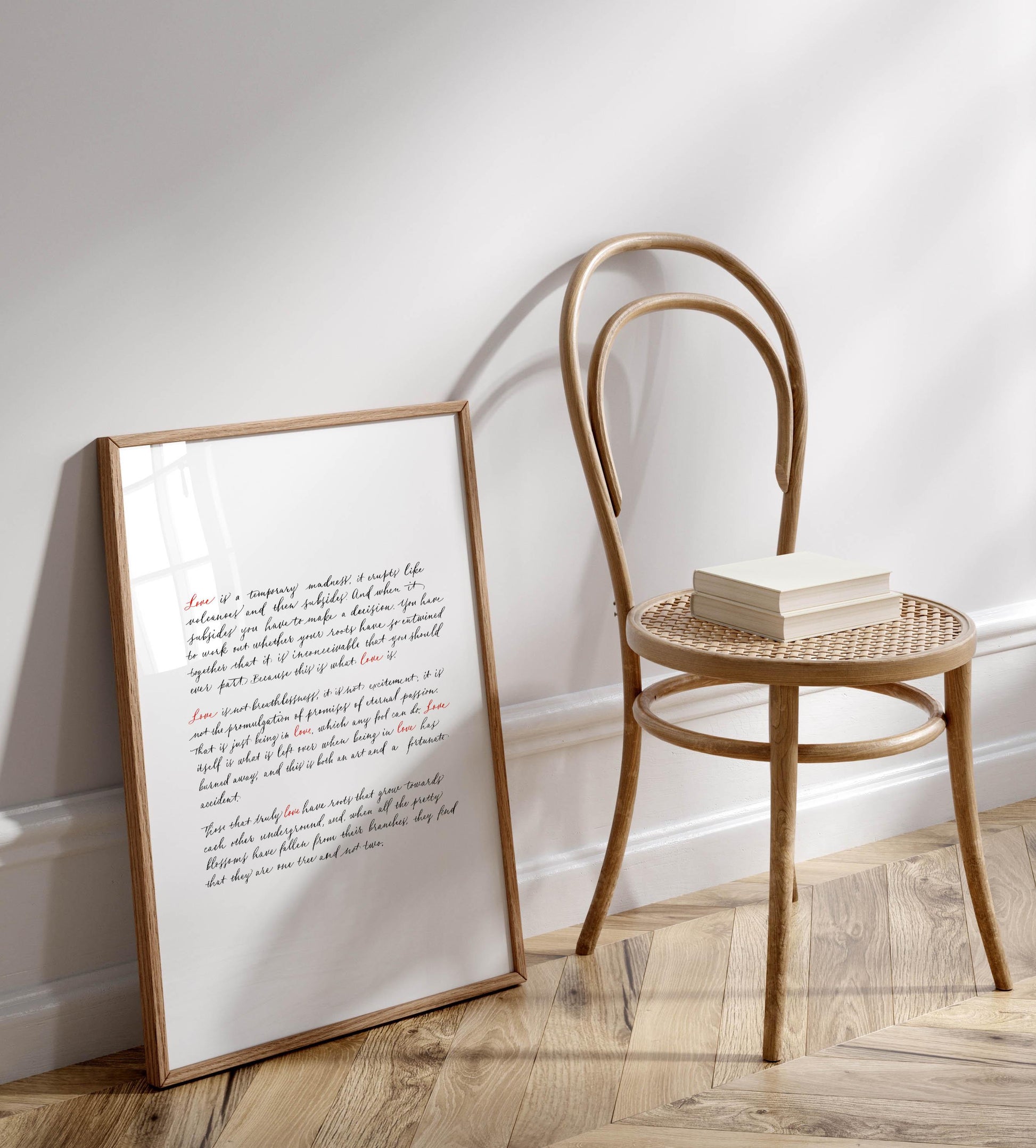 a wooden chair with a book resting on it, positioned next to a framed text on a white wall.
