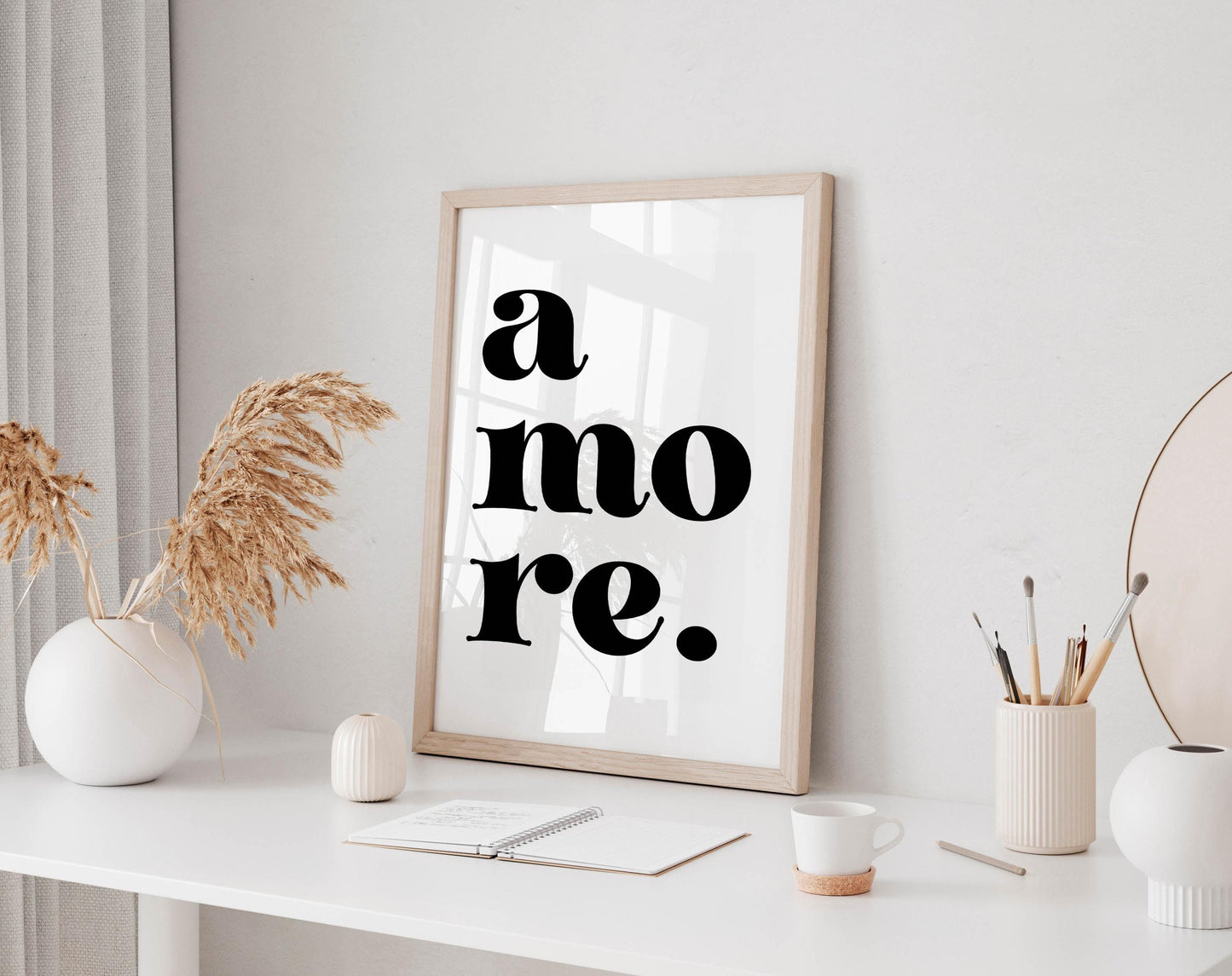 a minimalist workspace with a framed quote, a white desk, and various decorative elements such as a vase with dried flowers and a cup.