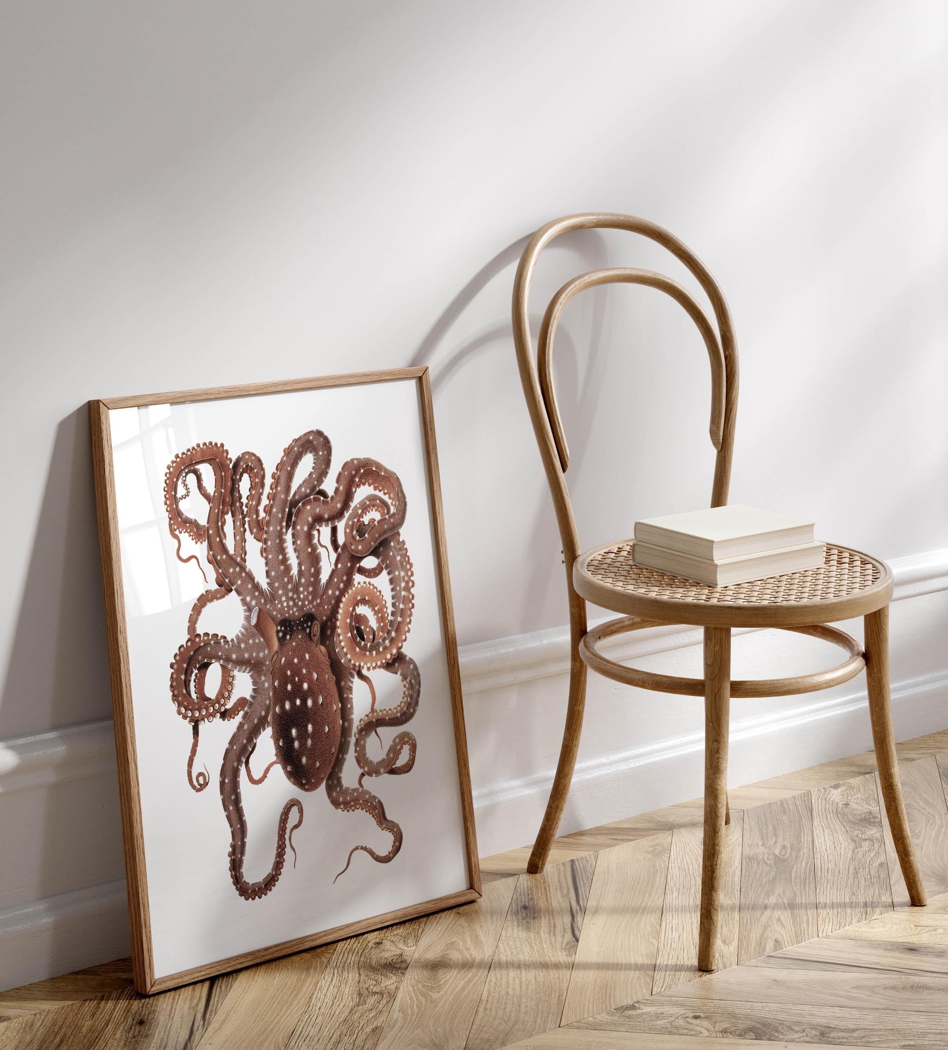 a framed illustration of an octopus, with its tentacles spread out, placed on a wooden floor next to a wooden chair.