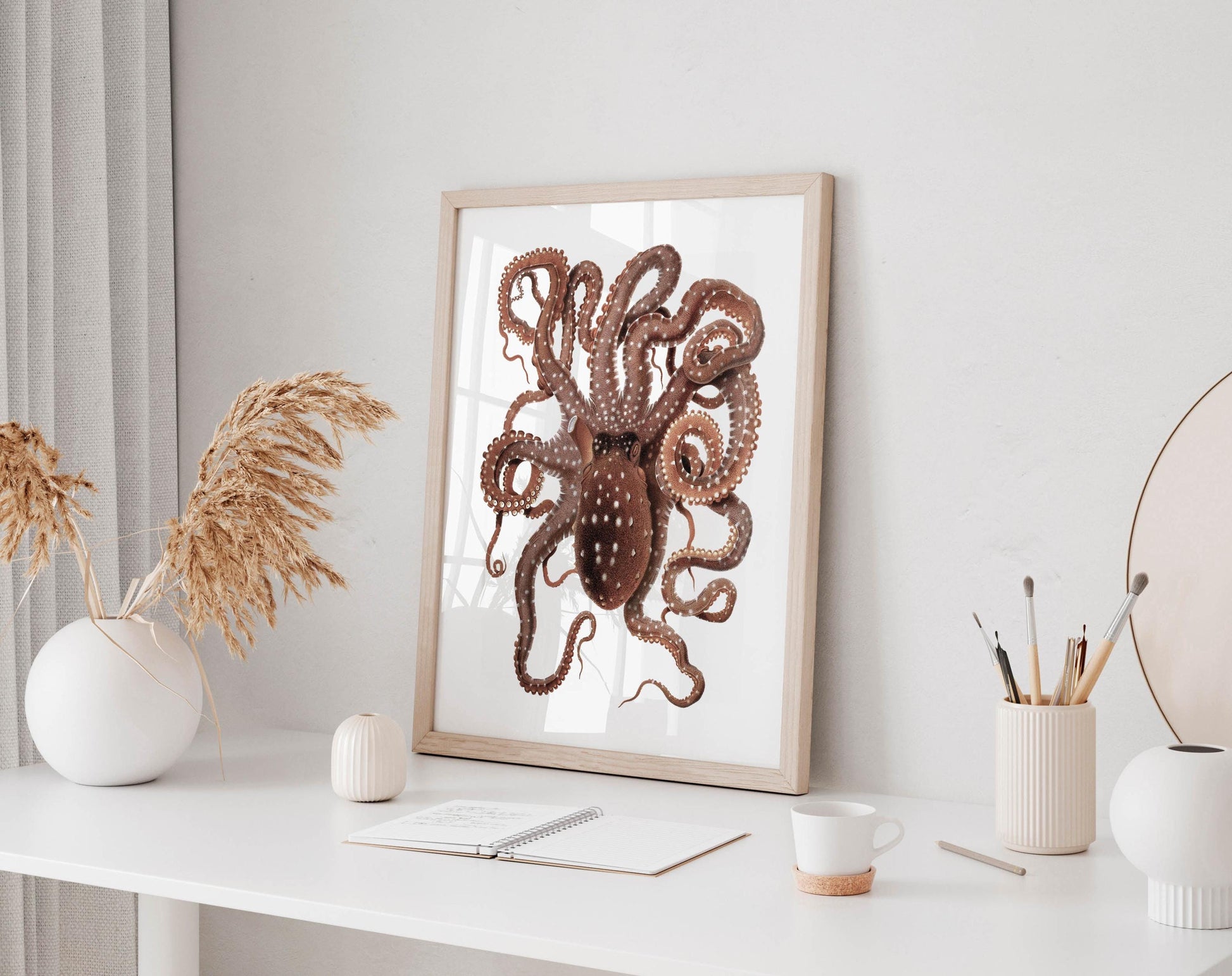 a framed picture of an octopus on a white desk, surrounded by various objects such as a notebook, a cup, and a vase.