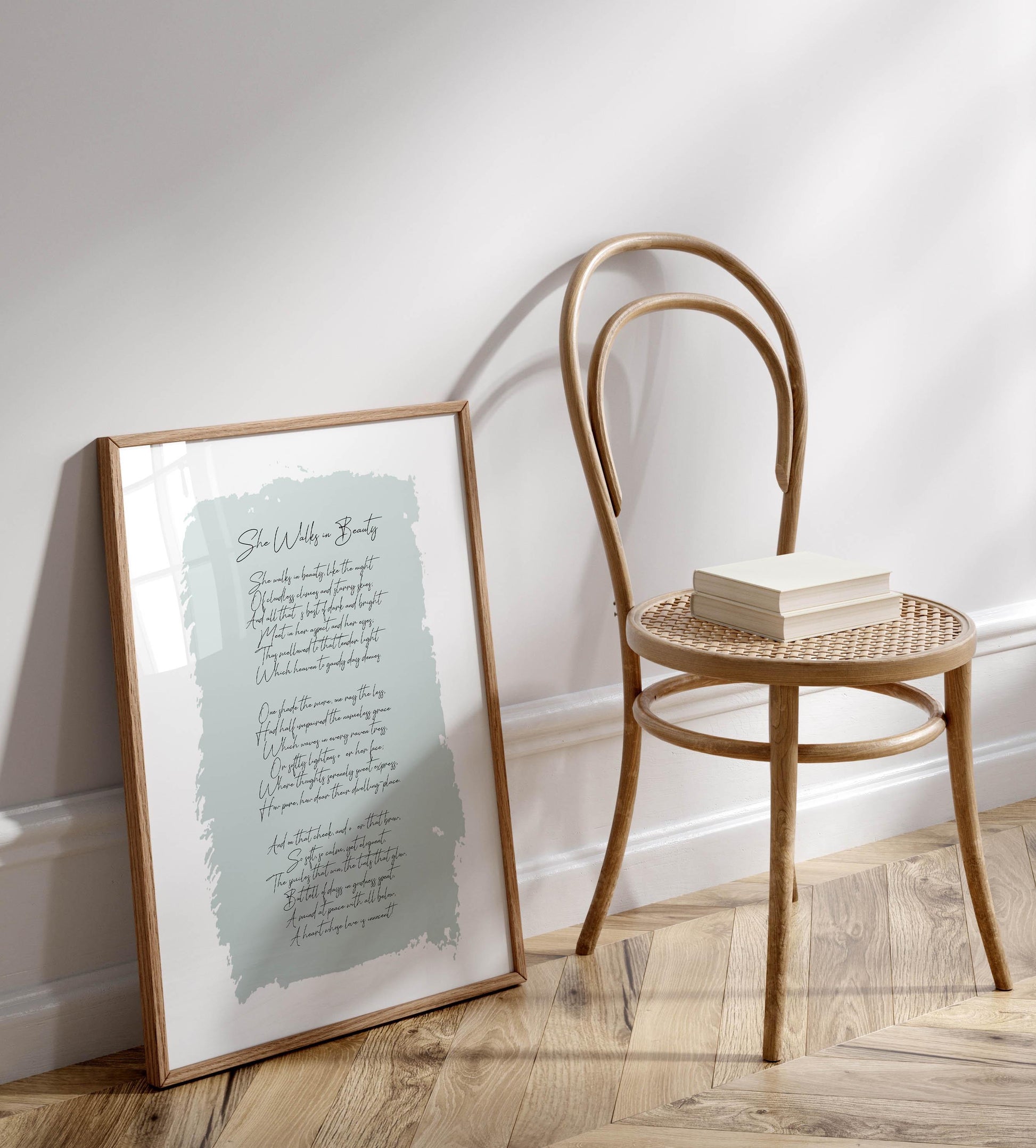 a framed print of a poem leaning against a wall, with a wooden chair and a stack of books placed next to it on a wooden floor.