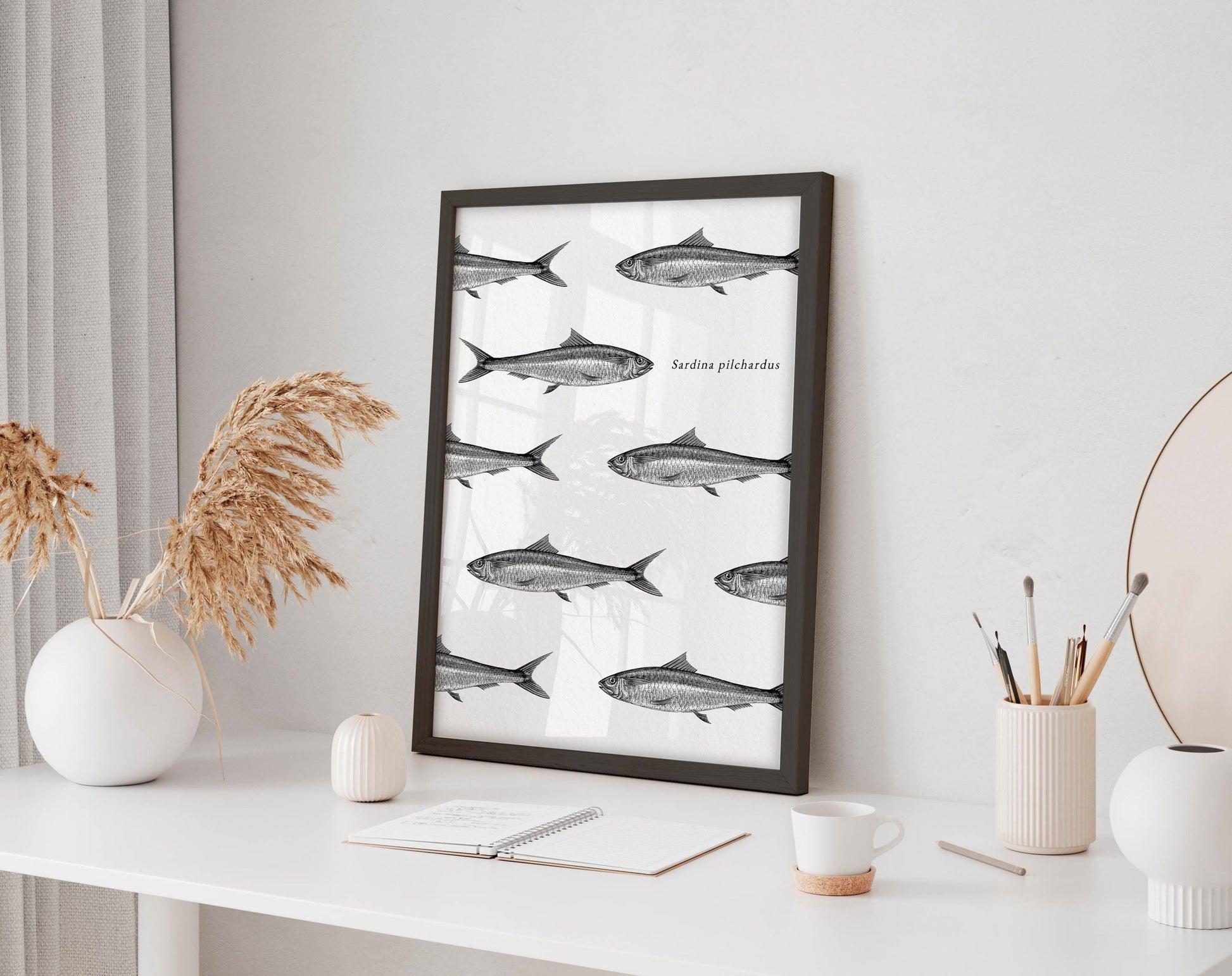 a framed poster of fish on a white wall, accompanied by a white desk with various items such as a notebook, a cup, and a vase.