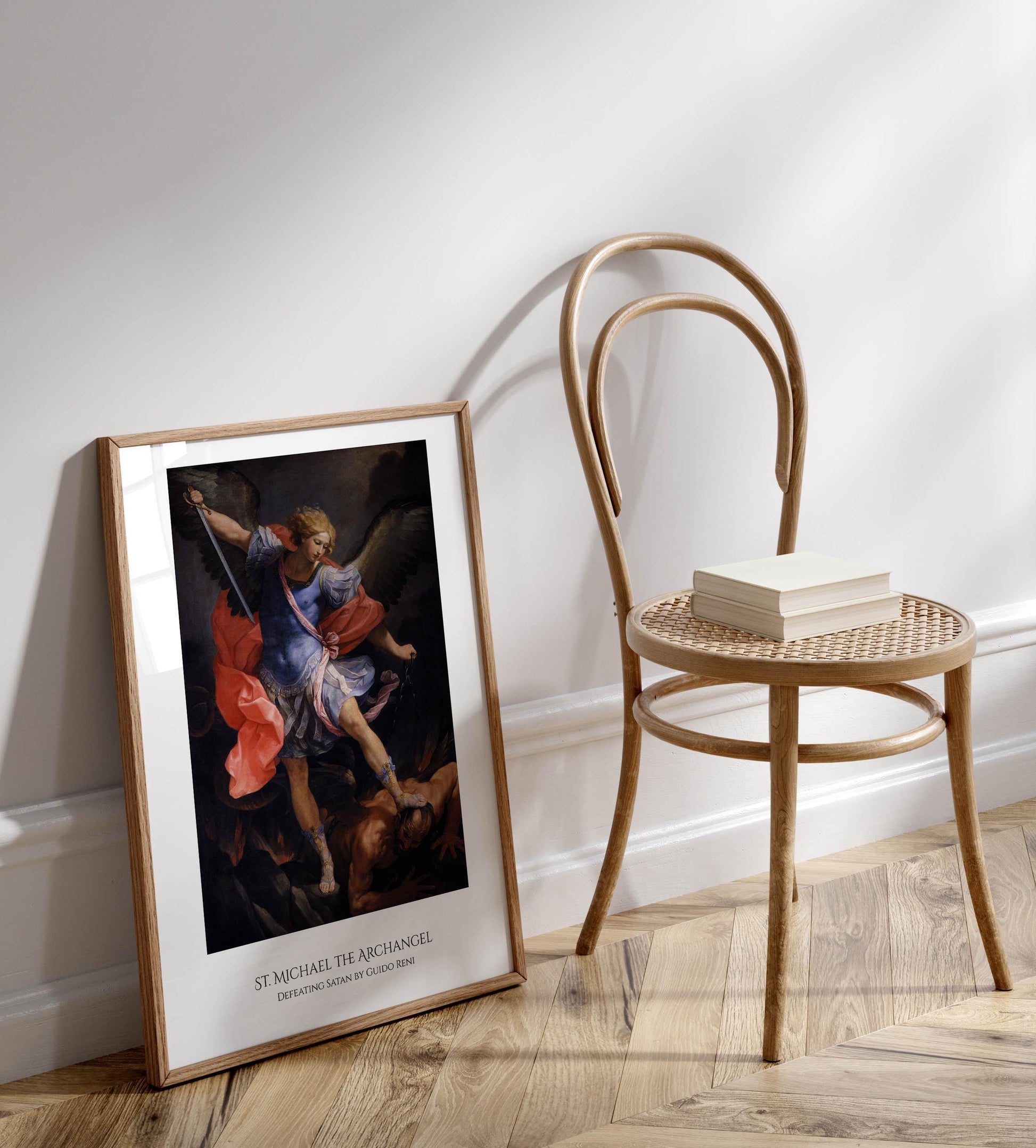 a framed painting of St. Michael the Archangel, a religious figure, standing on a pedestal and holding a sword. The painting is displayed on a wooden floor next to a wooden chair.