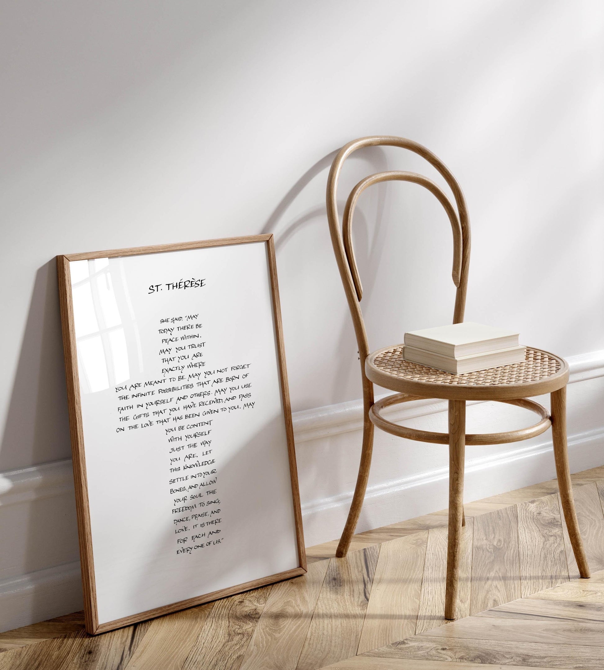 a framed poem titled "St. Therese" standing on a wooden floor next to a wooden chair.