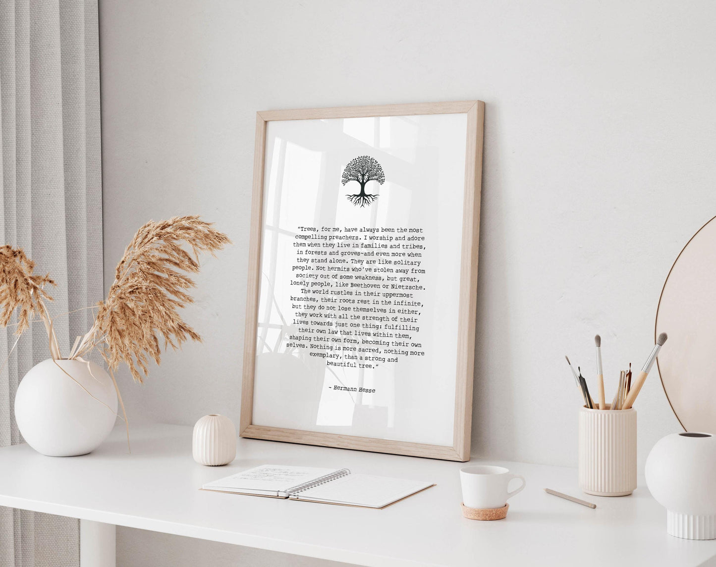 a framed quote with a tree symbol, placed on a white desk with various objects such as a notebook, a cup, and a vase.