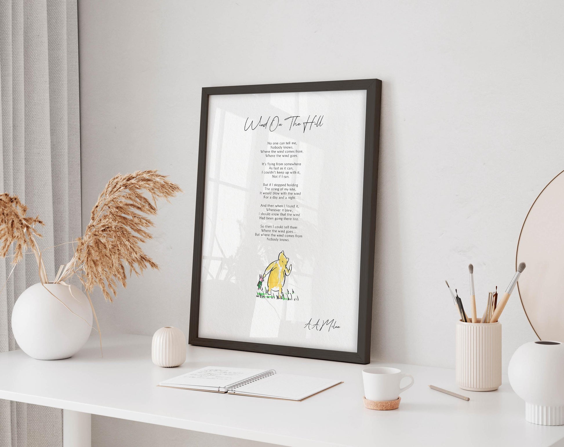 a framed poem titled "What's the Hill" displayed on a white desk, accompanied by a notebook, a cup, and a vase with dried flowers.