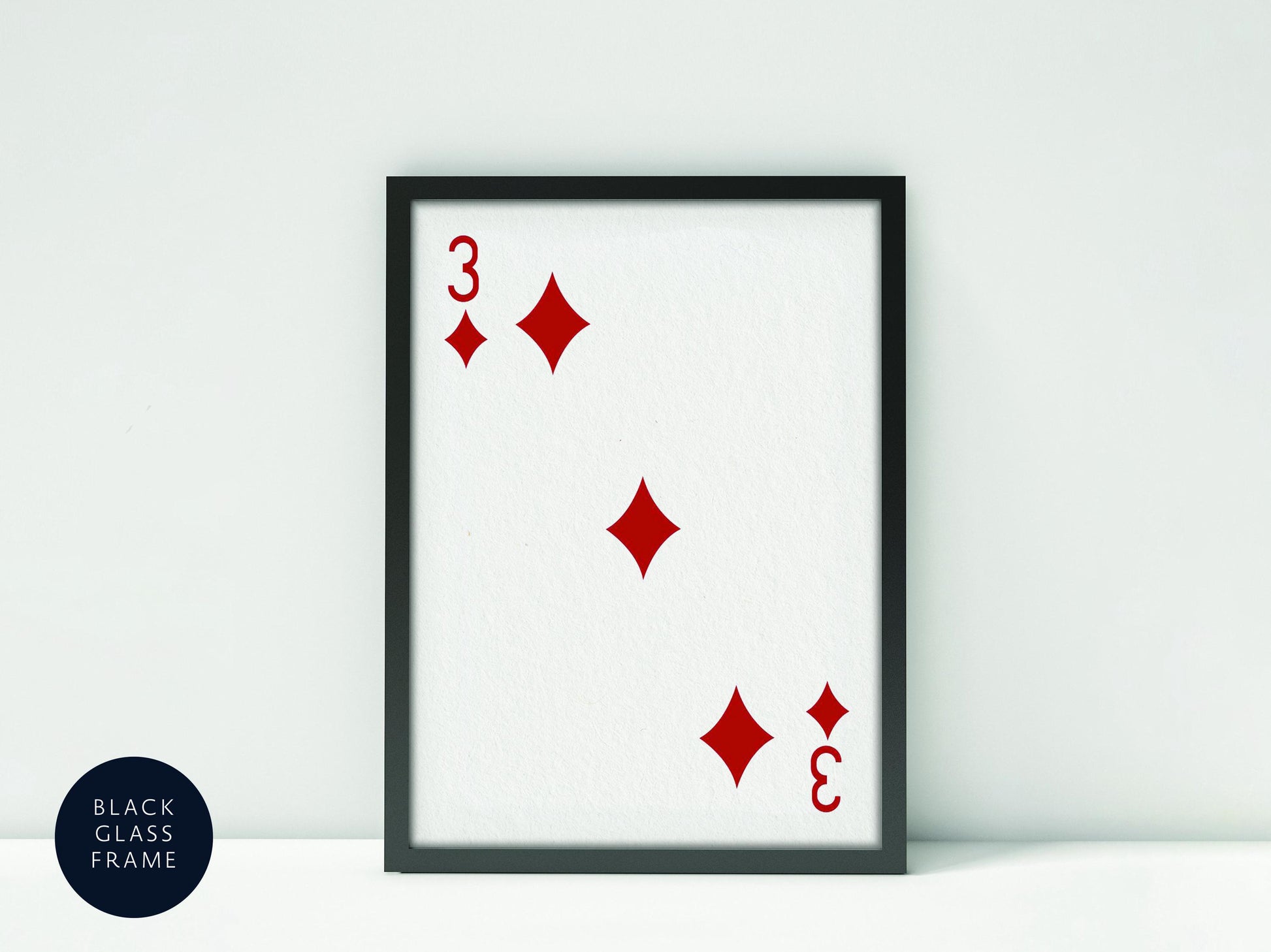 A framed print of a playing card with the number 3 and four diamonds on it, placed against a white background.