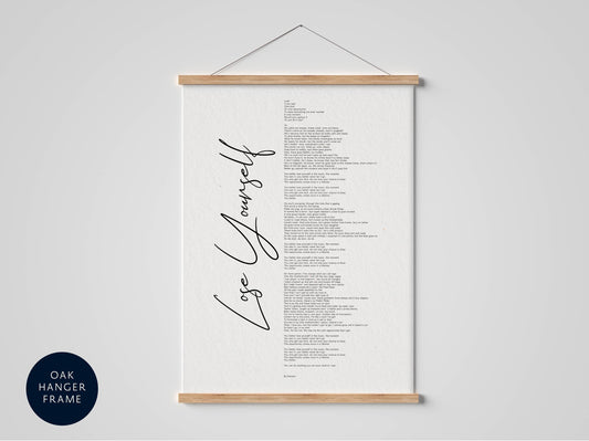 a poster with the phrase "Love Yourself" written on it in a cursive font. The poster is hanging on a wall, and there is a wooden hanger frame below it.