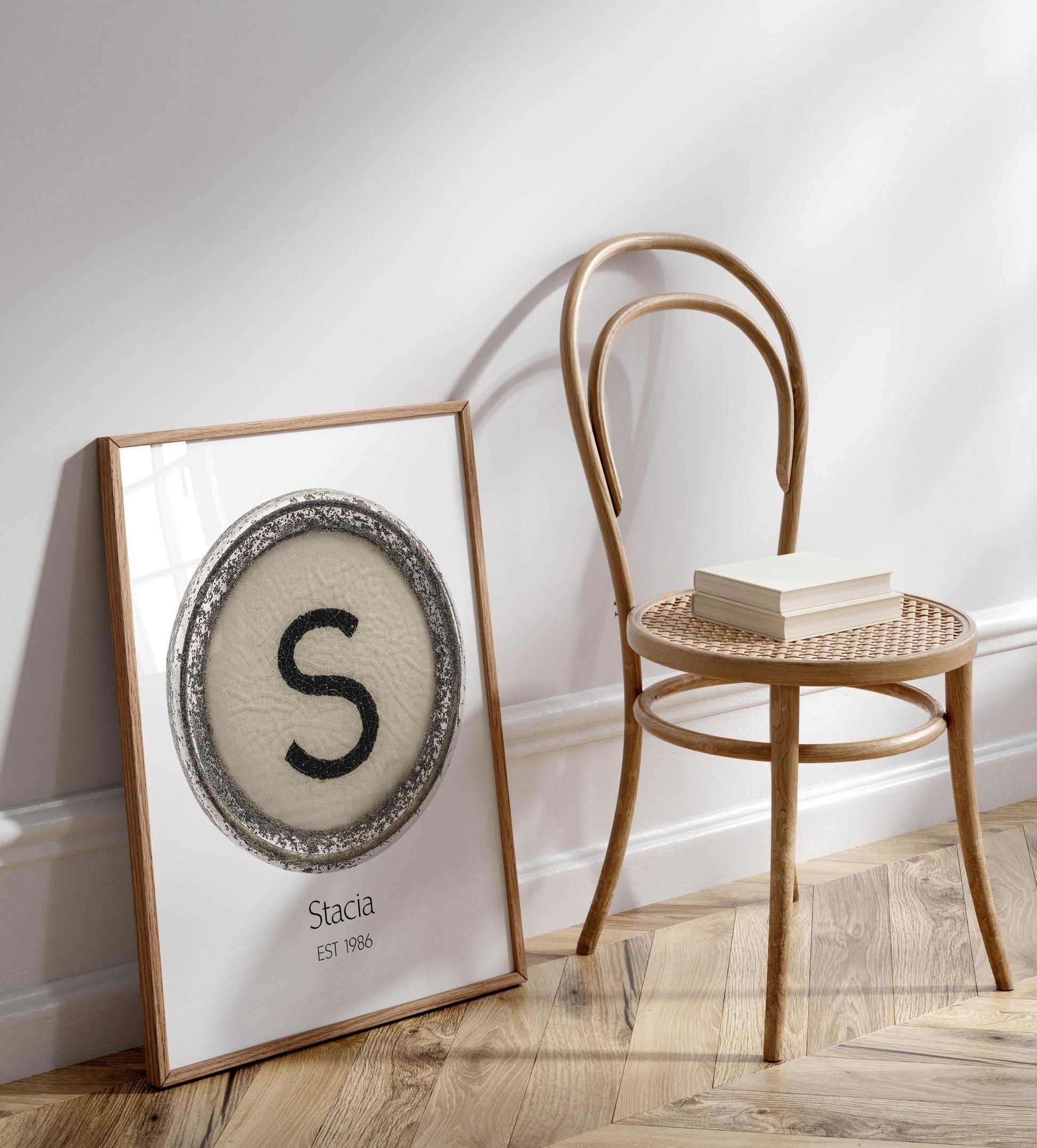 a framed poster with a large letter 'S' on it, placed on a wooden floor next to a wooden chair.