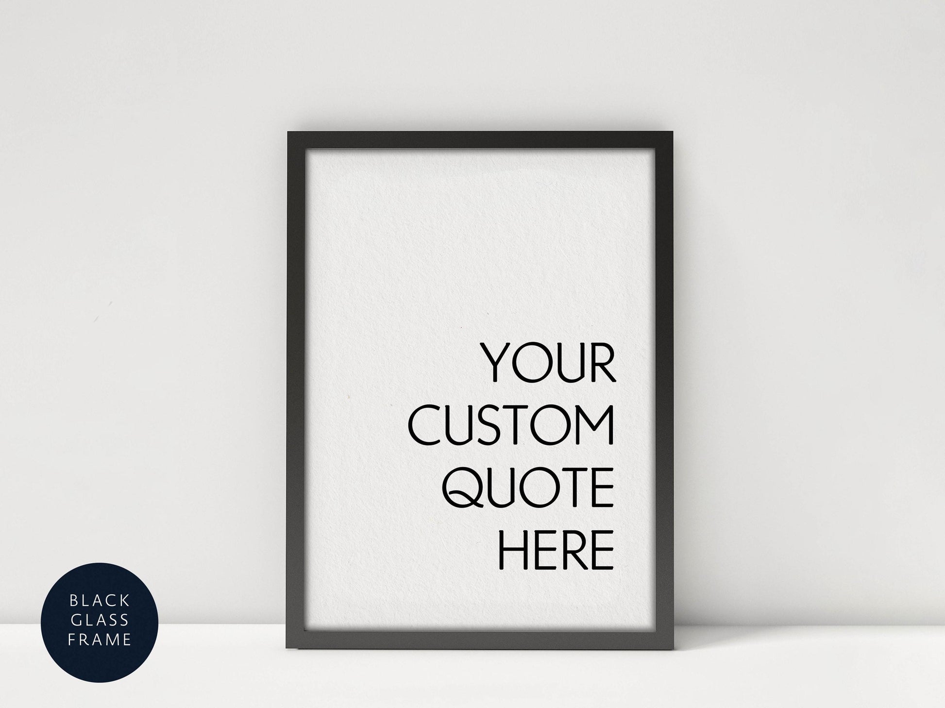 A black framed poster with the text "YOUR CUSTOM QUOTE HERE" displayed on it, placed against a white wall.