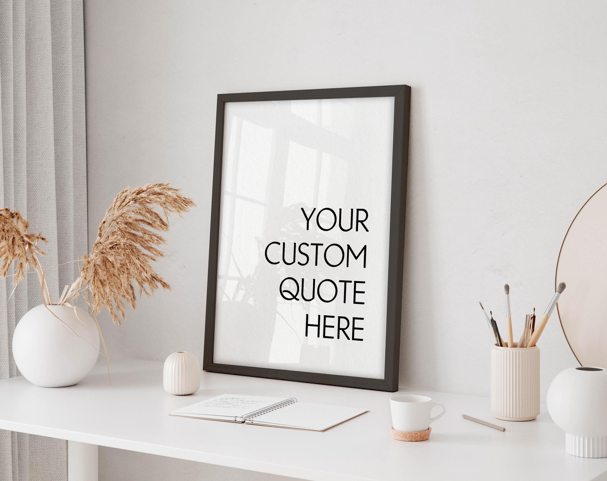 a white desk with a framed quote that reads "YOUR CUSTOM QUOTE HERE" in bold black text. The desk also has a few decorative items, including a vase with dried flowers, a small white candle, and a white mug.
