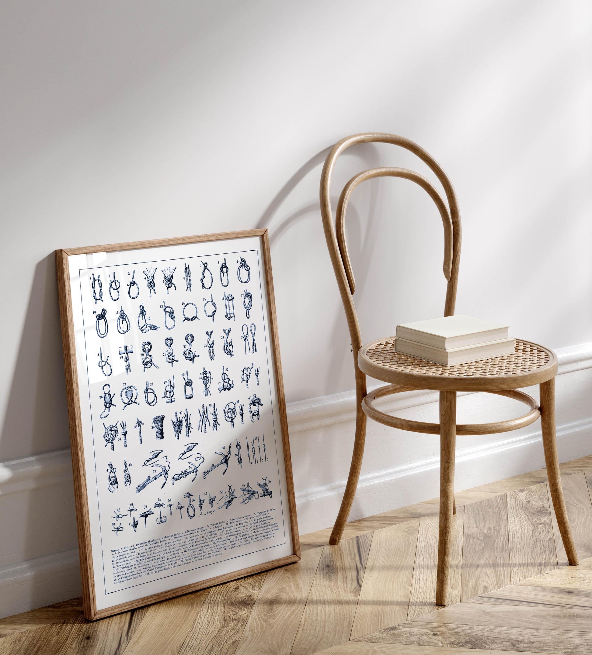 a wooden chair with a book resting on it, placed against a white wall. There is a framed poster or collage of various illustrations or symbols on the wall next to the chair.