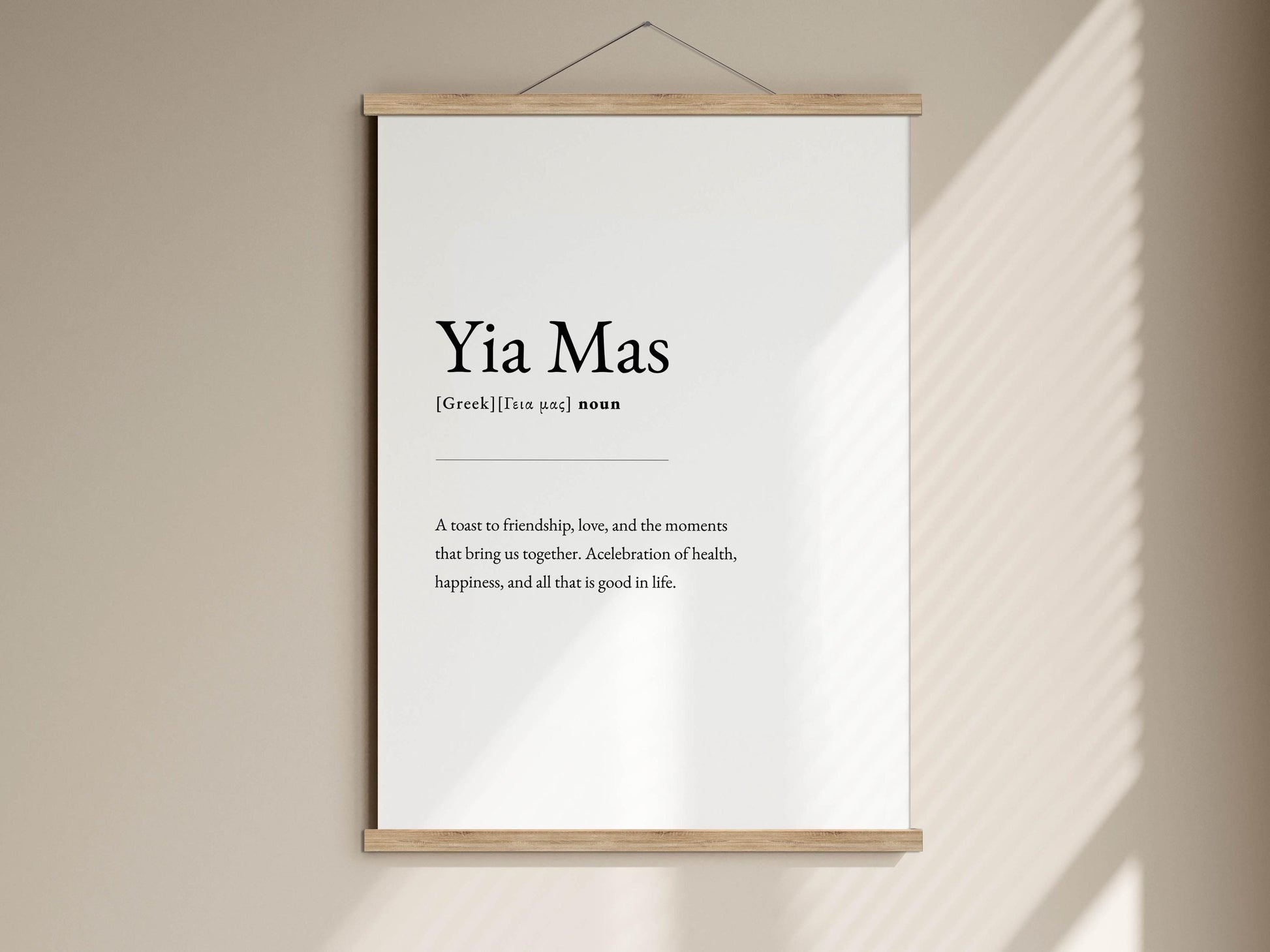 A white poster with black text hanging on a wall, displaying the definition of 'Yia Mas' as a sense of friendship, love, and the moments that bring people together.
