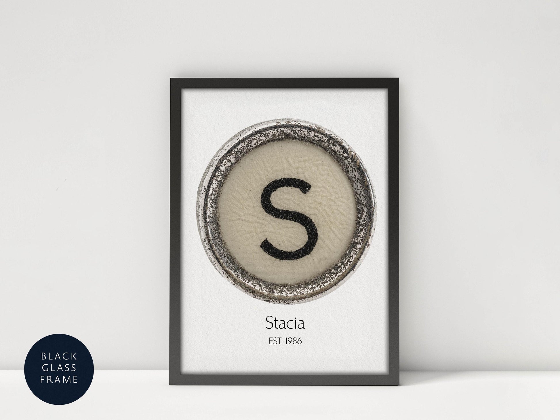 a framed print with a circular design containing the letter 'S' in the center, and the text "Stacia EST 1986" below the design.