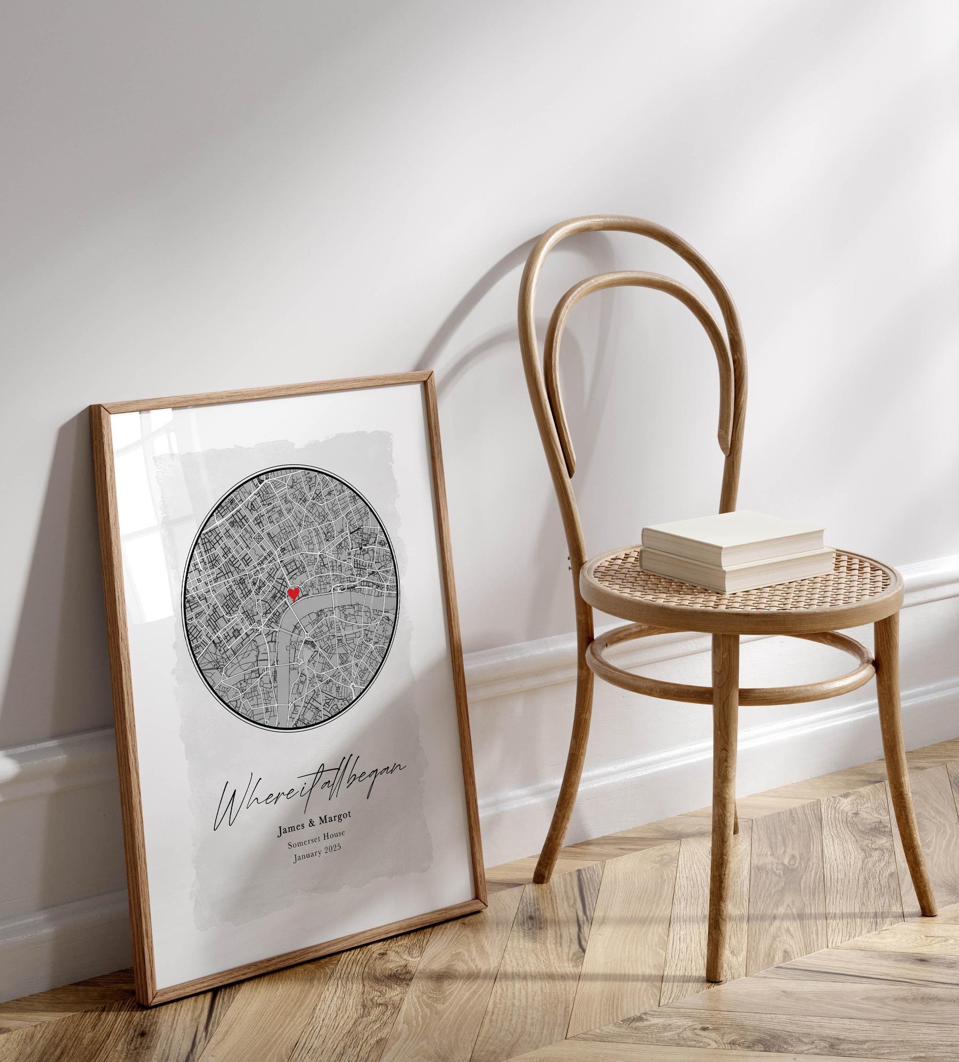 a framed map of London with a book and a wooden chair placed next to it on a wooden floor.