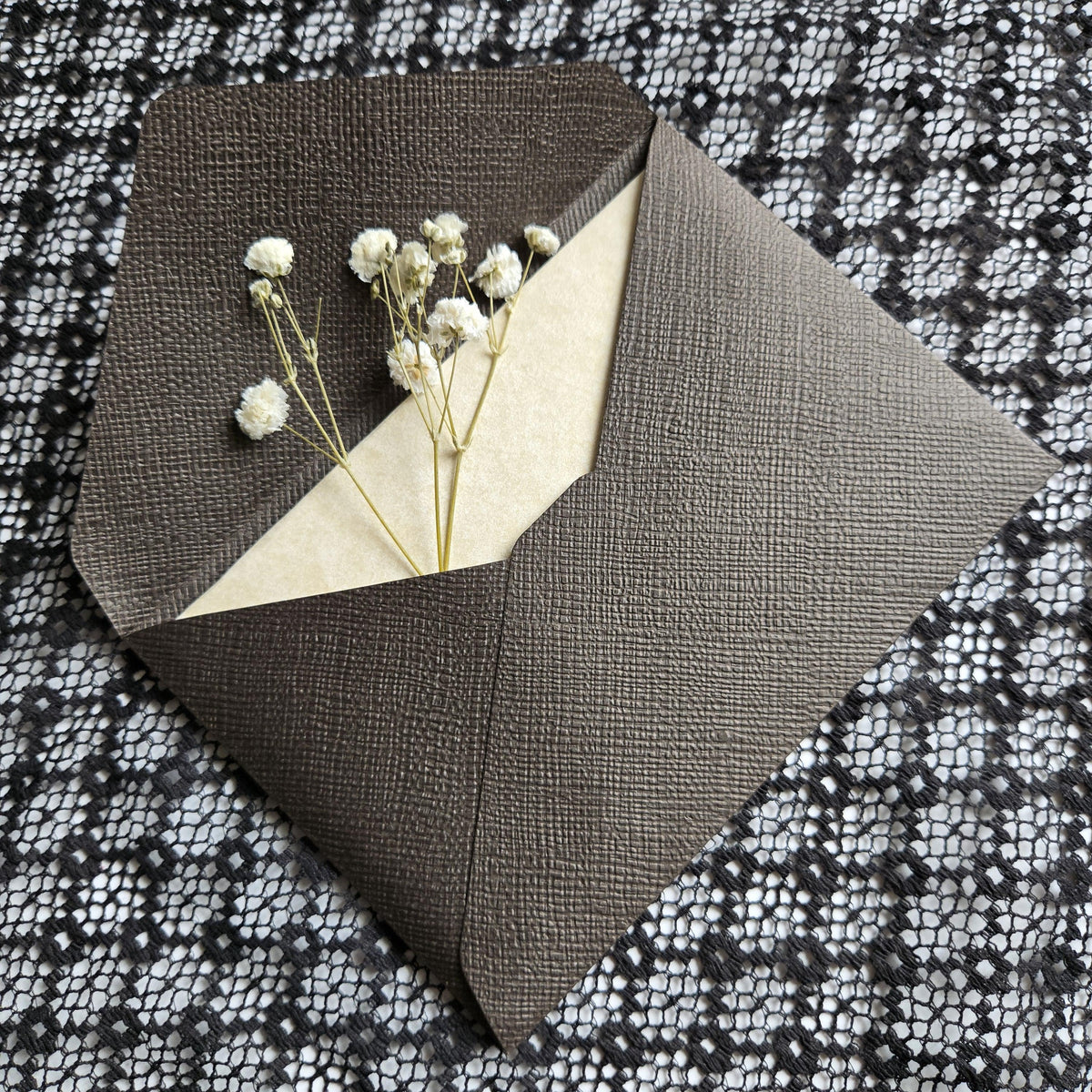 a small bouquet of white flowers placed inside an envelope, which is resting on a black and white patterned fabric.
