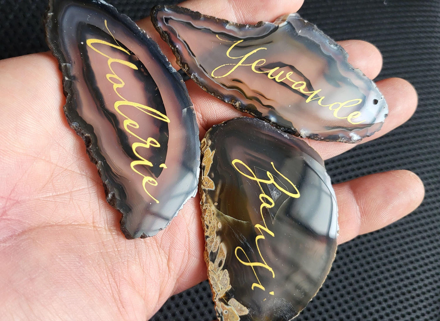 A hand holding three unique rock slices with names written on them.