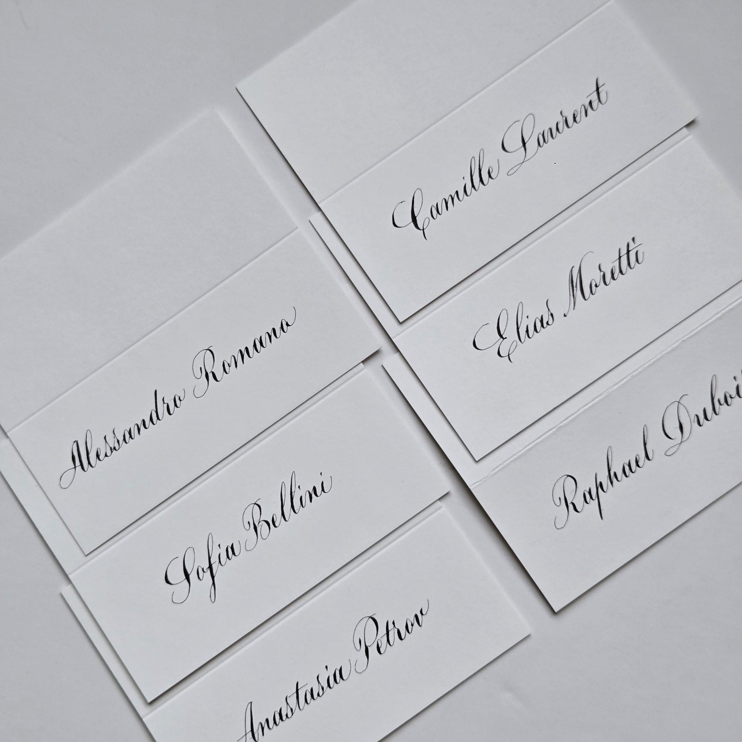 several white name cards with black cursive text, likely for a formal event or gathering.
