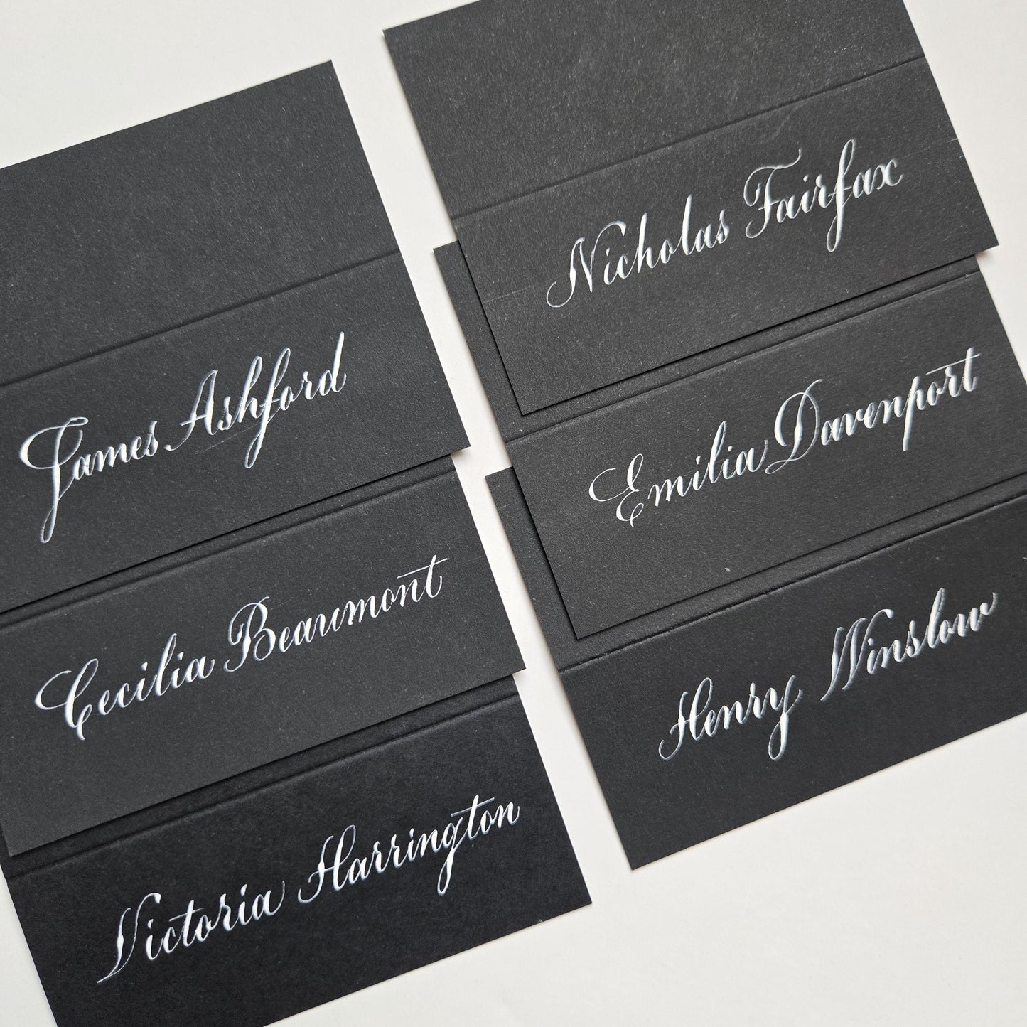 a collection of black name cards with handwritten names on them, arranged in two rows.