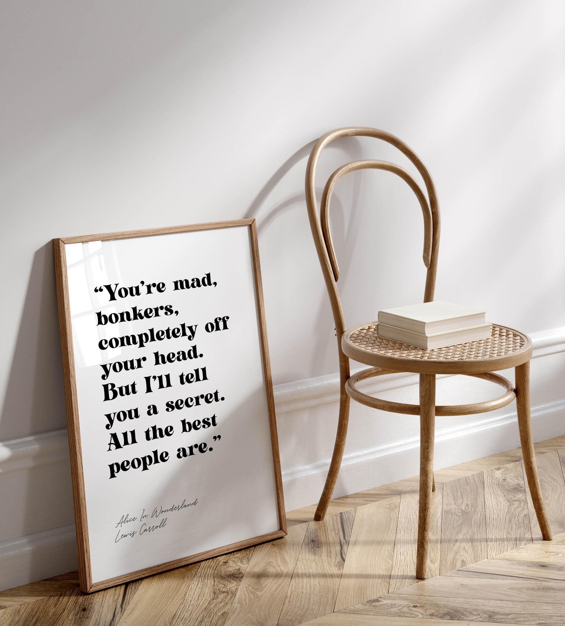 a framed quote on a wall next to a wooden chair, with a book on the chair&#39;s seat.