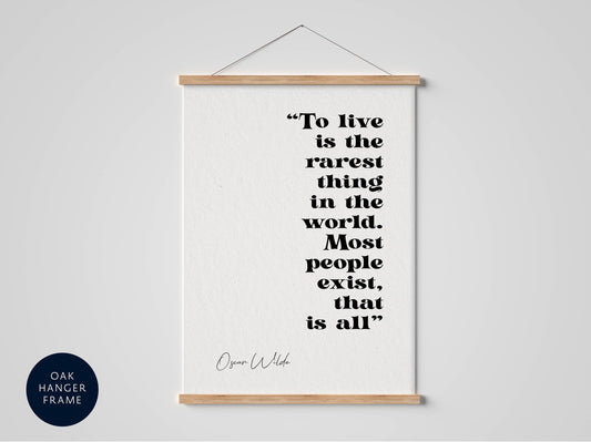 a quote by Oscar Wilde that reads &quot;To live is the rarest thing in the world. Most people exist, that is all.&quot; The quote is presented in a black and white style, and it is hanging on a white wall.