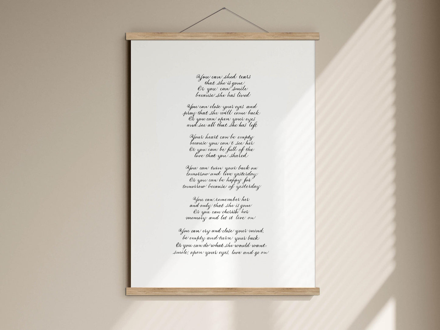 a white poster with black text, which appears to be a poem or lyrics. The text is written in a cursive font and is displayed on a wooden frame. The poster is hung on a wall, and the background is a simple beige color.