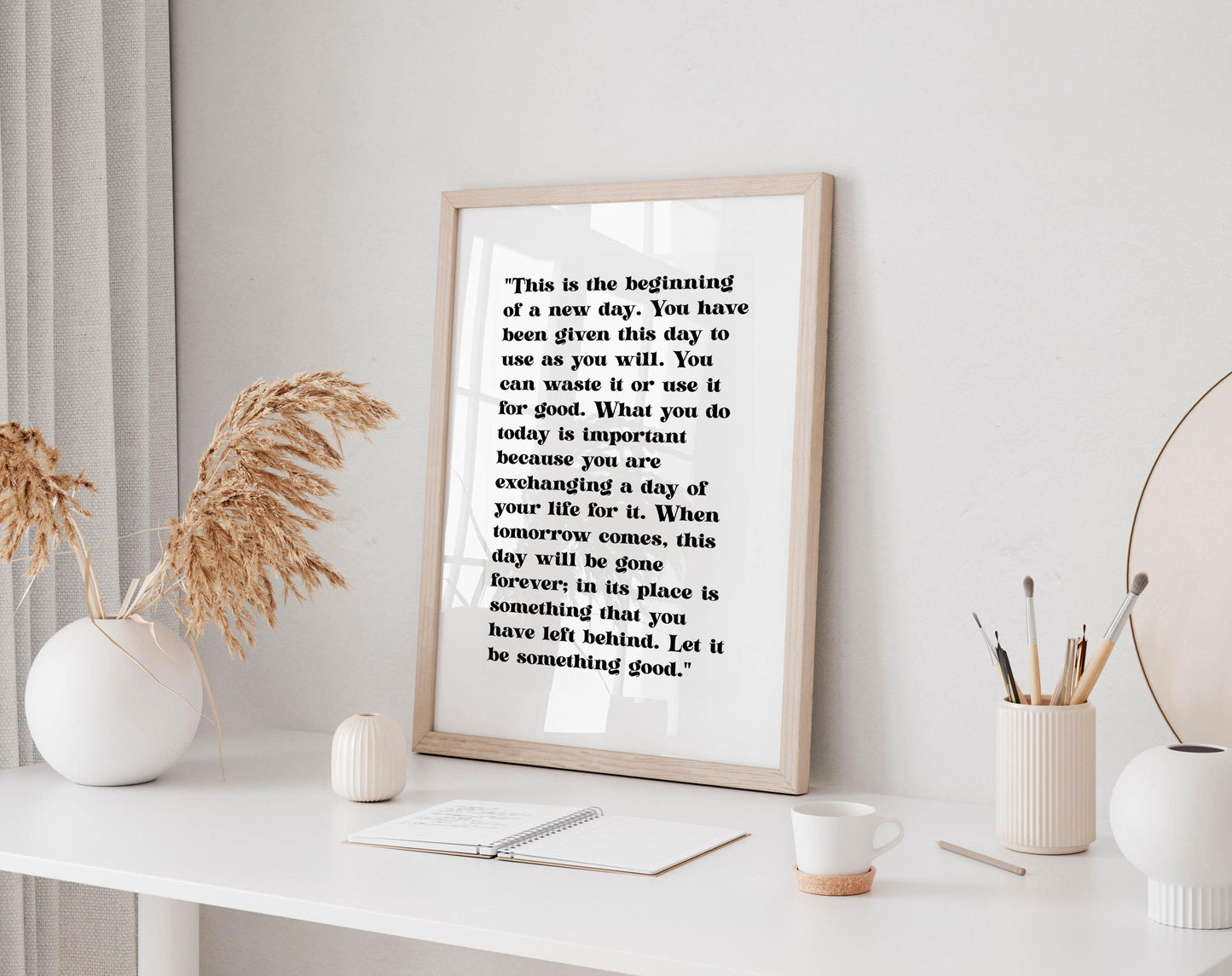 a framed quote on a white shelf, surrounded by various objects such as a white vase, a white mug, and a white plant.