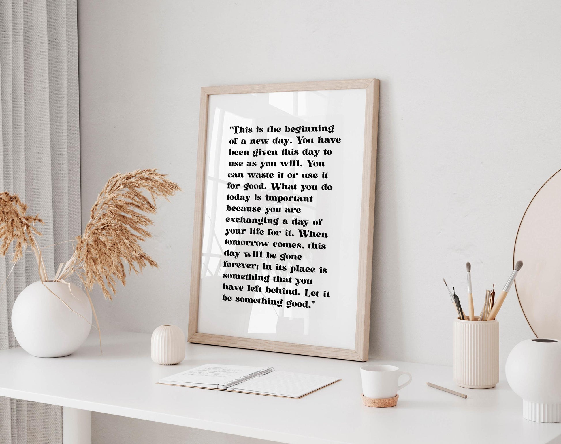 a framed quote on a white shelf, surrounded by various objects such as a white vase, a white mug, and a white plant.